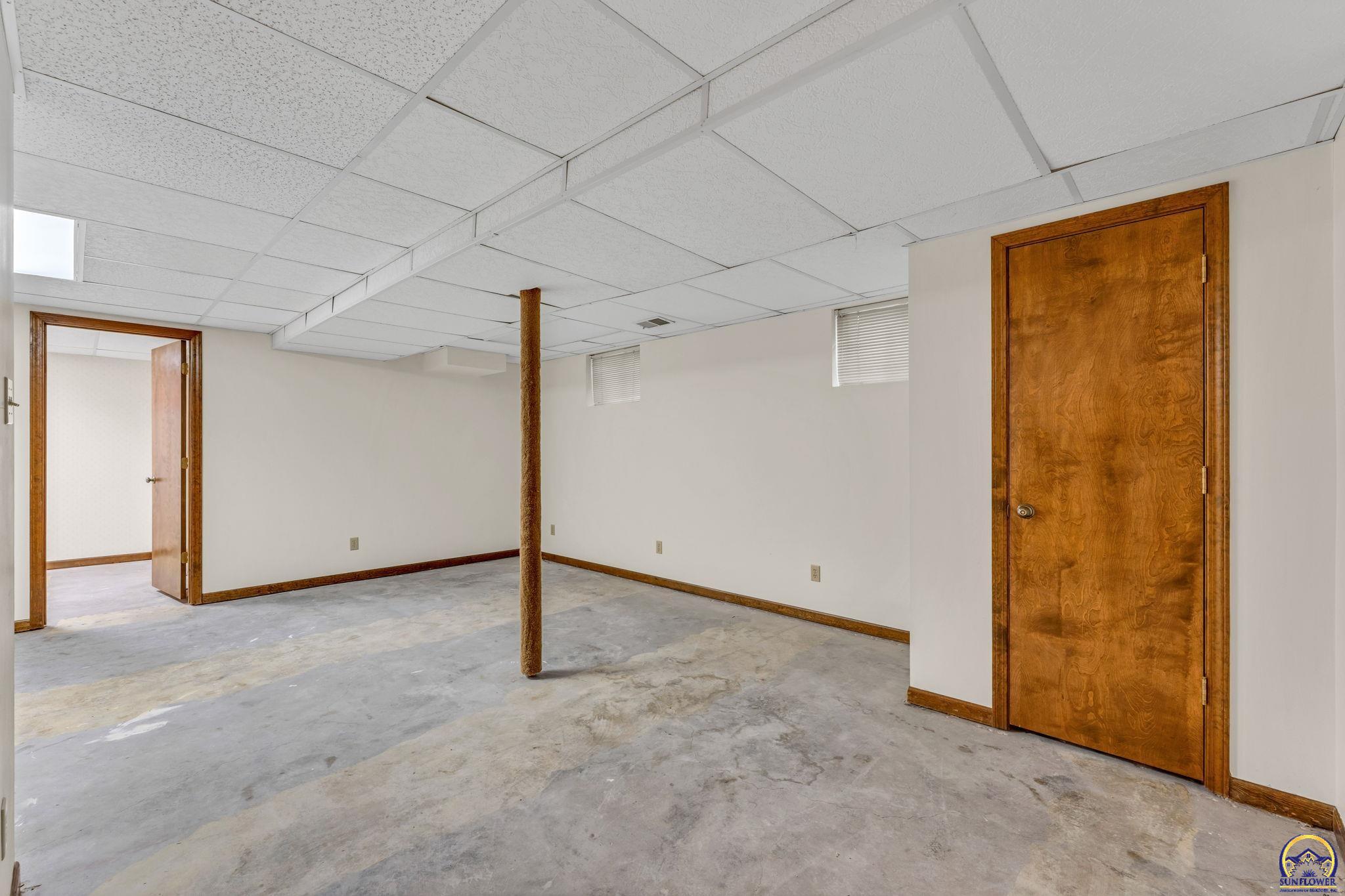 Empty basement with a concrete floor, drop ceiling, and central support post.