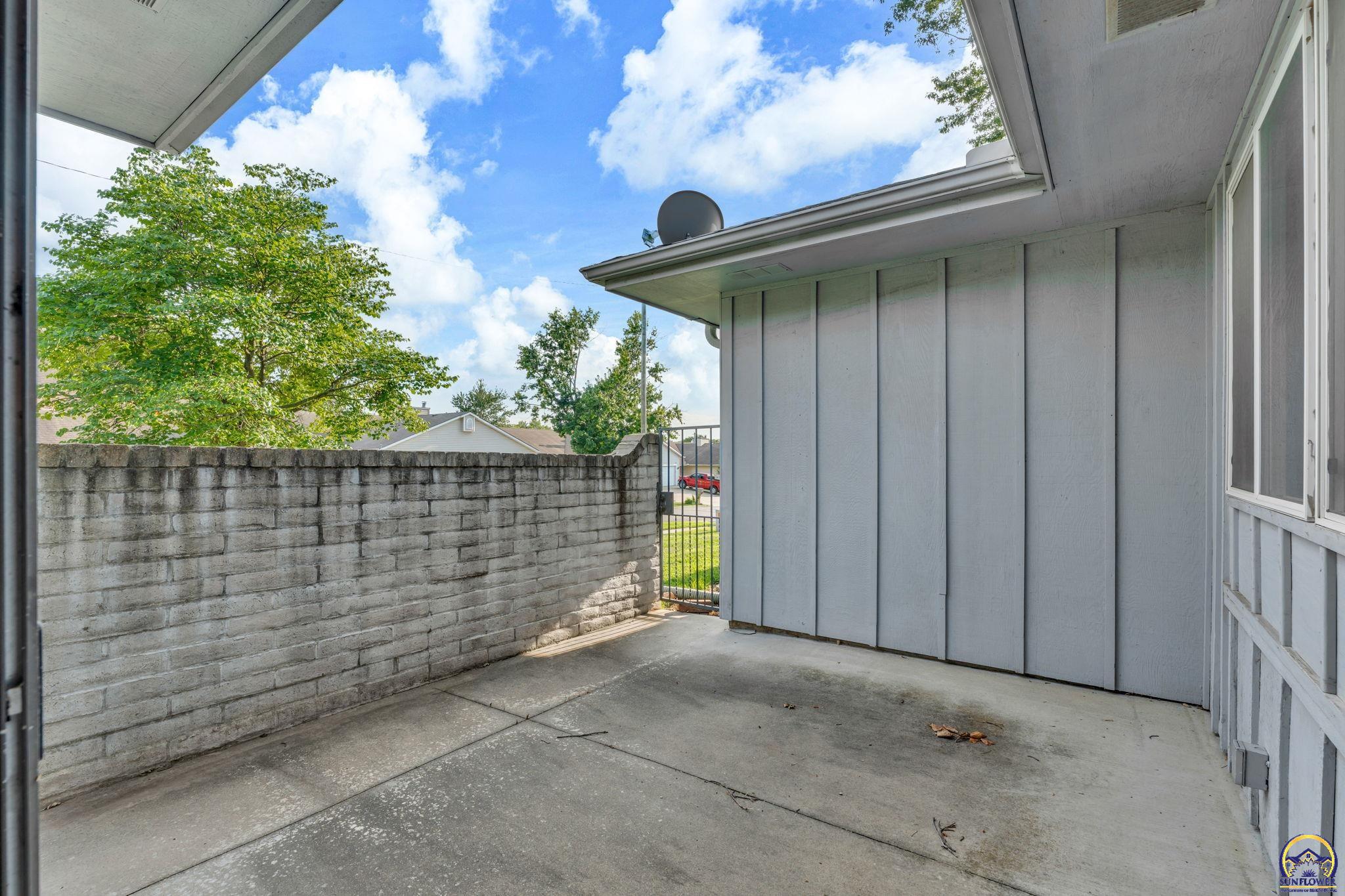 Covered concrete patio with a cinder-block wall and metal gate.
