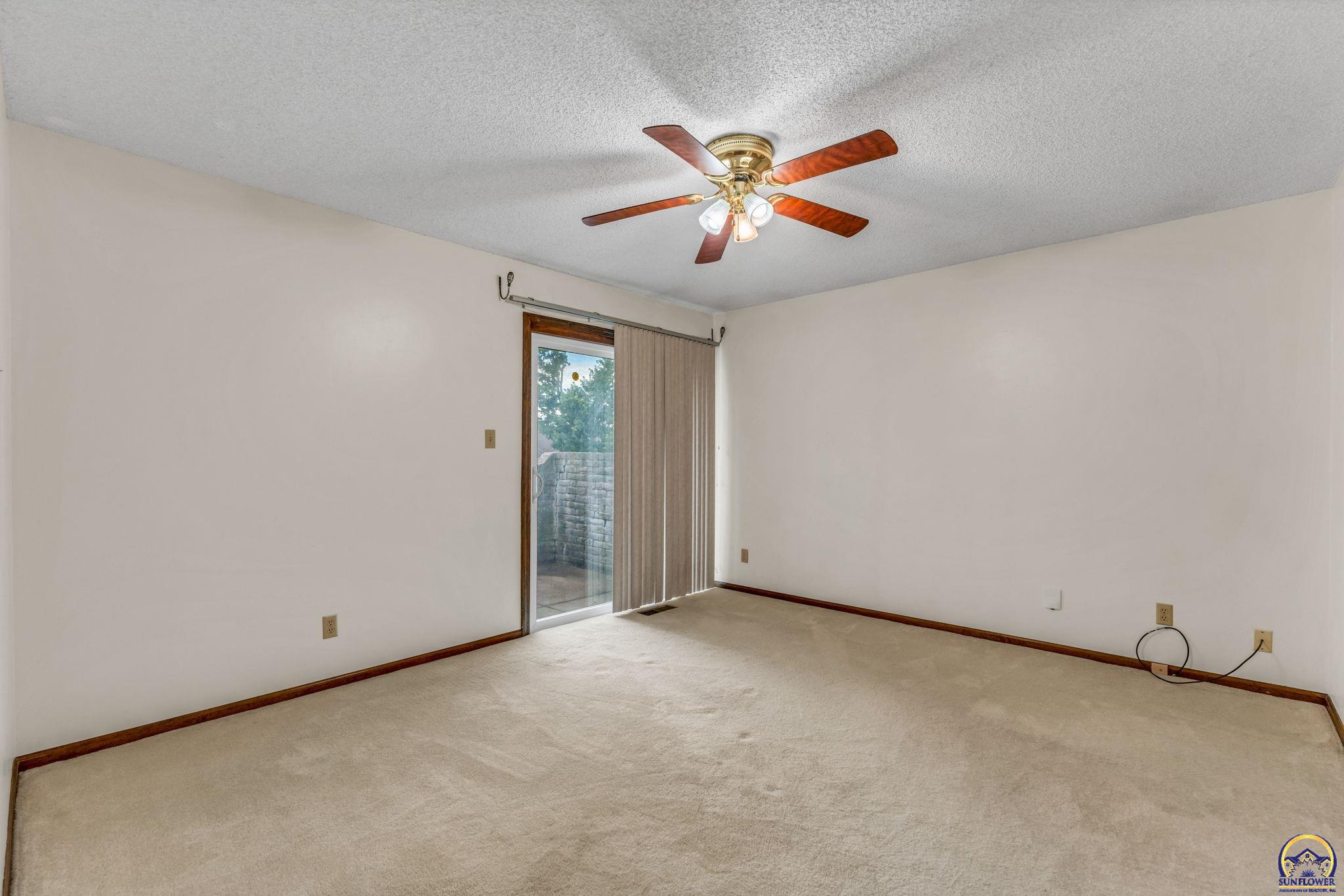 Empty carpeted room with a ceiling fan and sliding glass door to a patio.