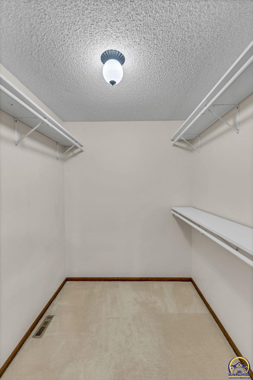 Empty walk-in closet with white shelving on both sides and beige carpet.
