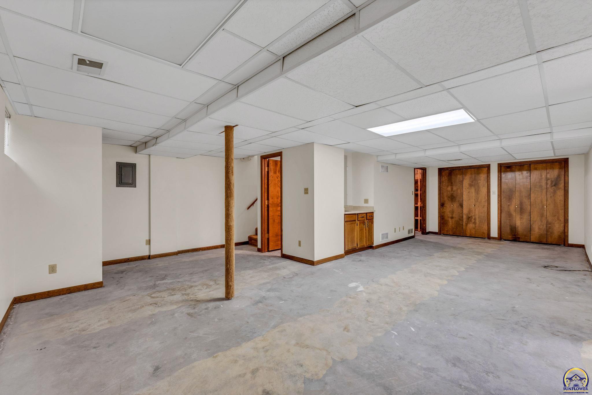 Unfinished basement with a concrete floor, wooden closet doors, and a small kitchenette.