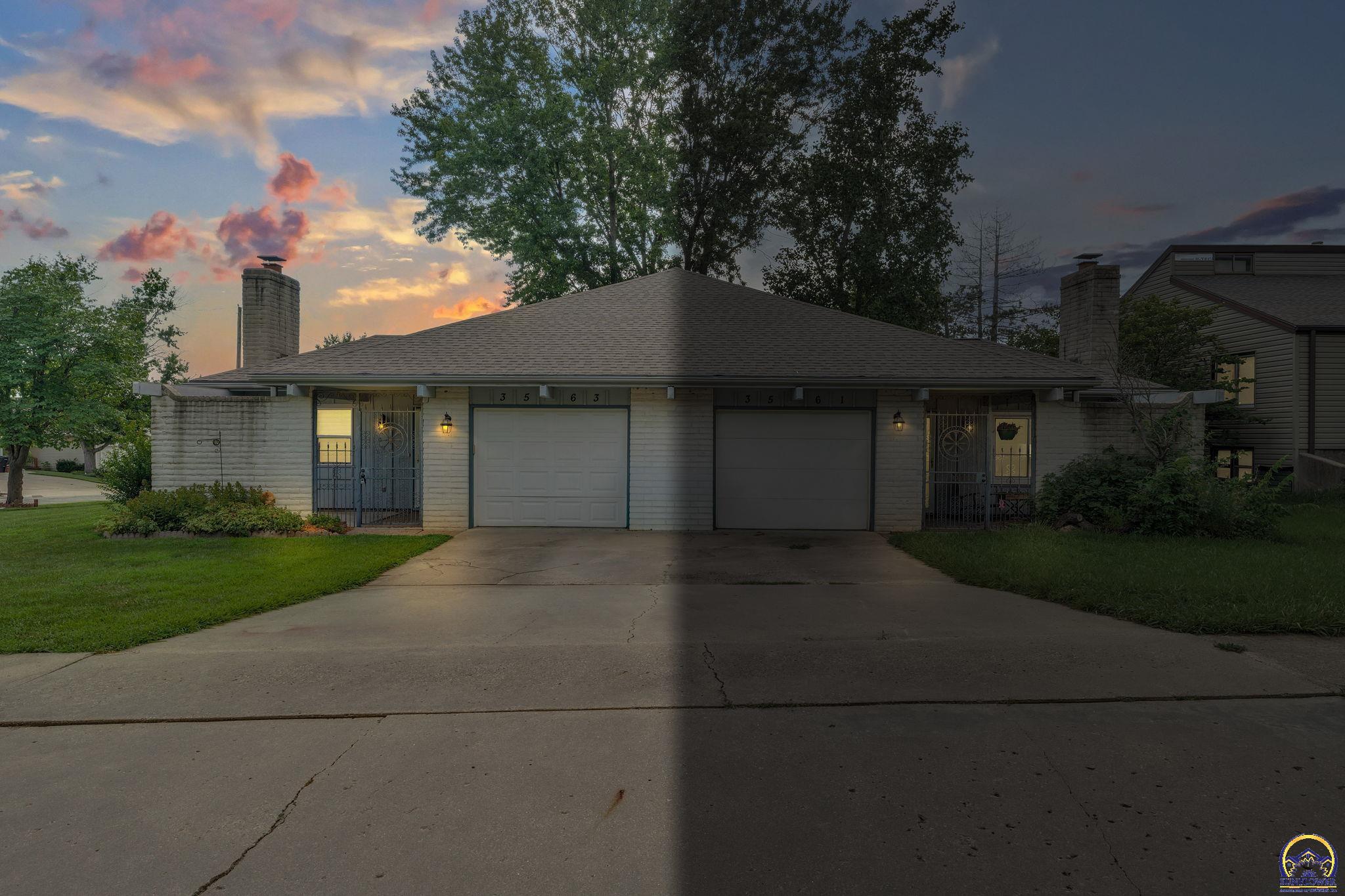 Single-story brick home with two garage doors and a broad driveway at dusk.
