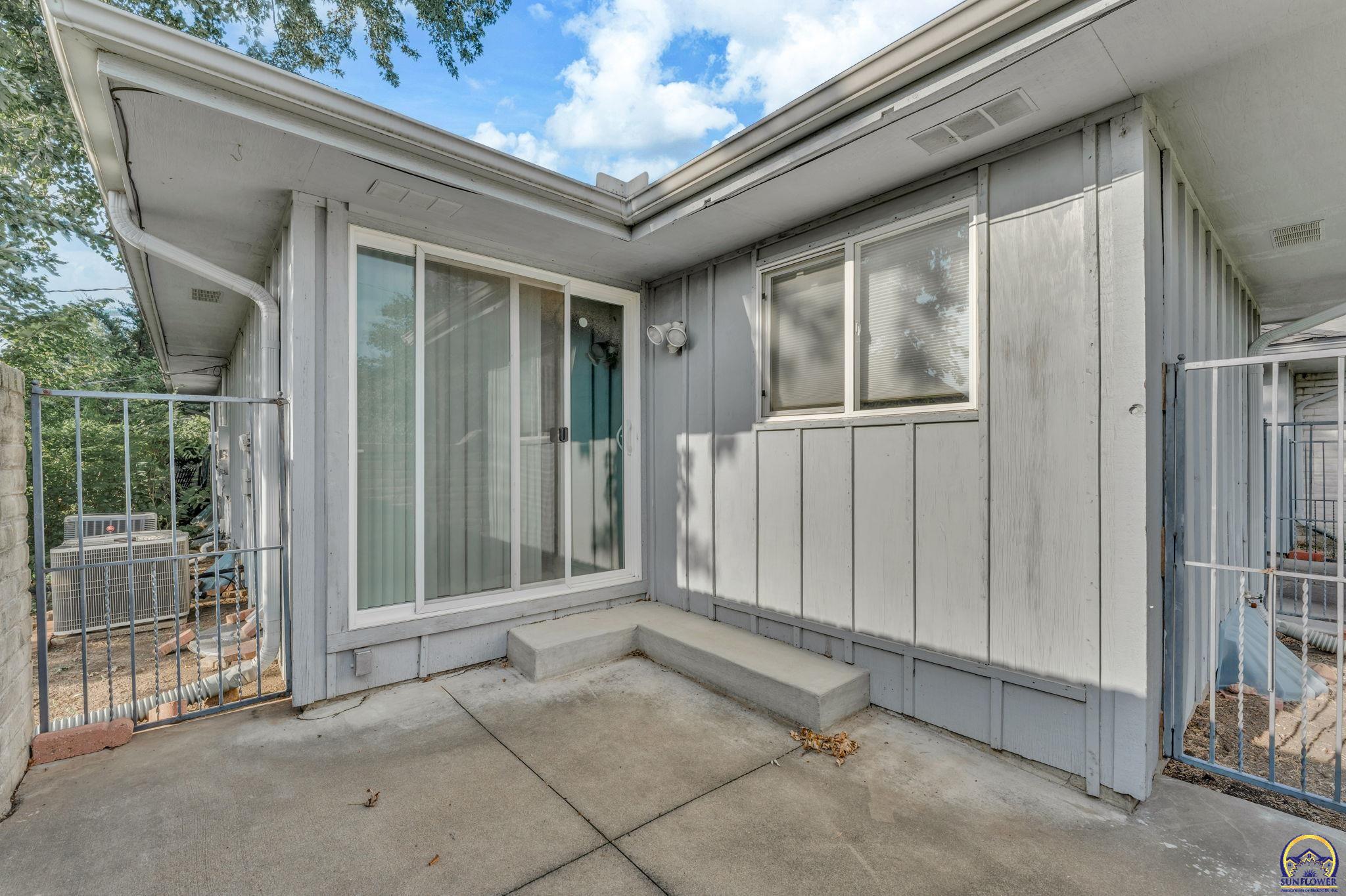 Concrete patio beside a gray-sided home, with a sliding glass door and metal railings.
