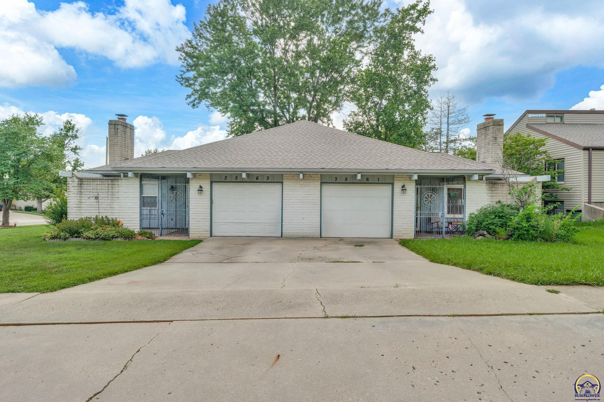Light-brick duplex with two garage doors, separate gated entrances, and a wide concrete driveway.