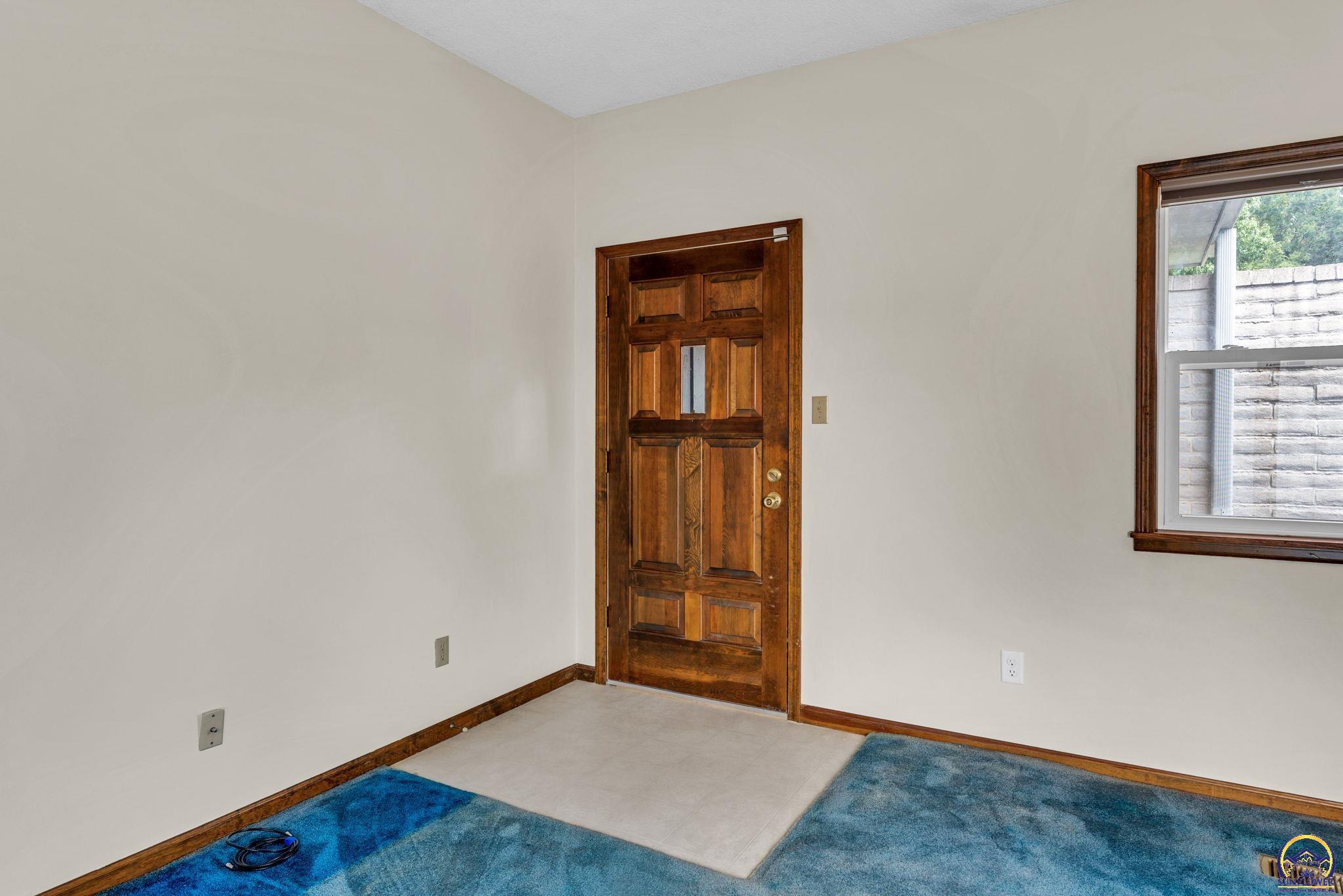 Entryway with a paneled wooden front door, blue carpet, and a tiled floor by the entrance.