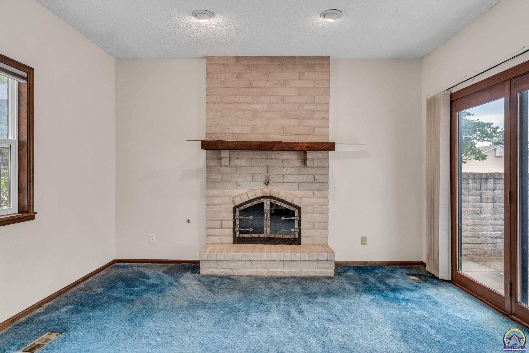 Unfurnished living room with a pale brick fireplace, dark wood mantel, and blue carpet.