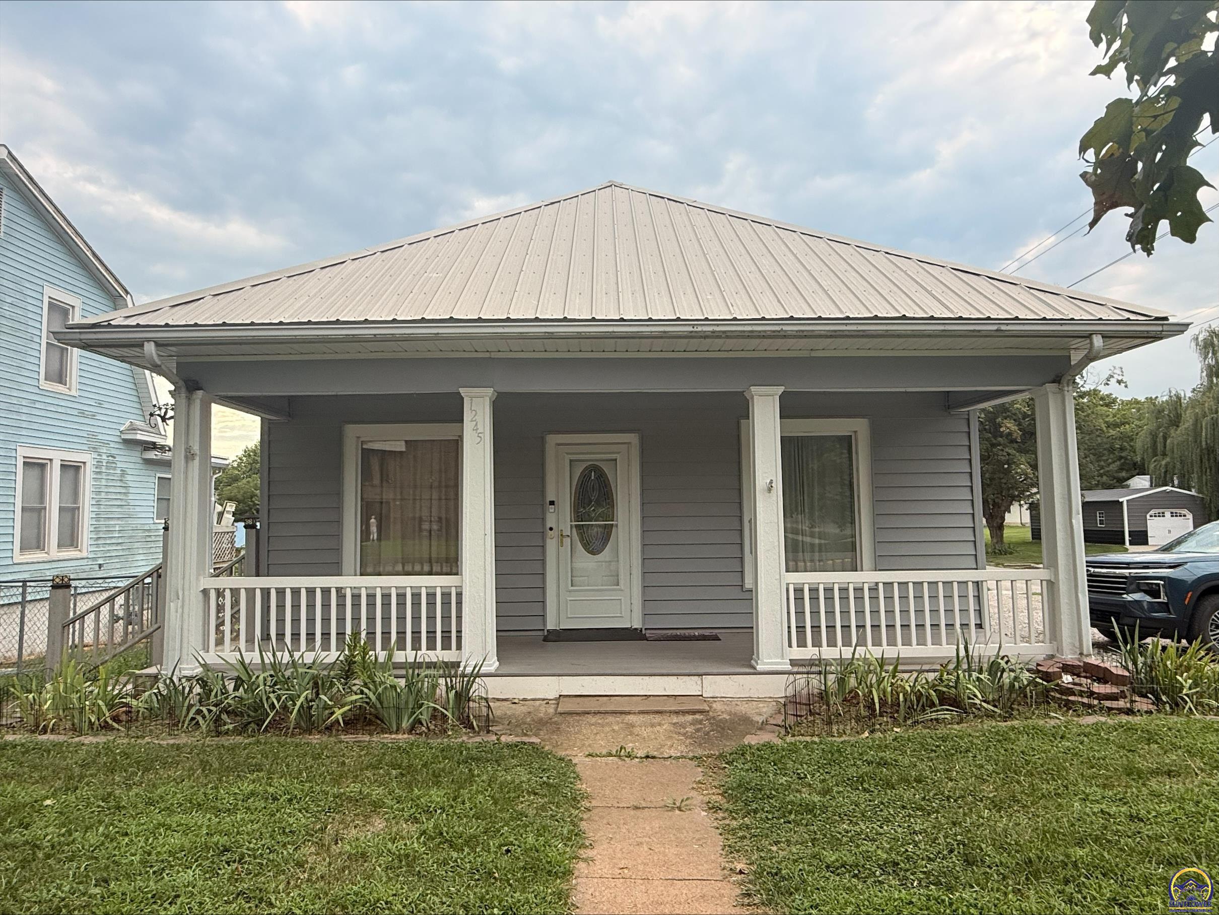 Gray house with a broad covered porch, white railings, and a light metal roof.
