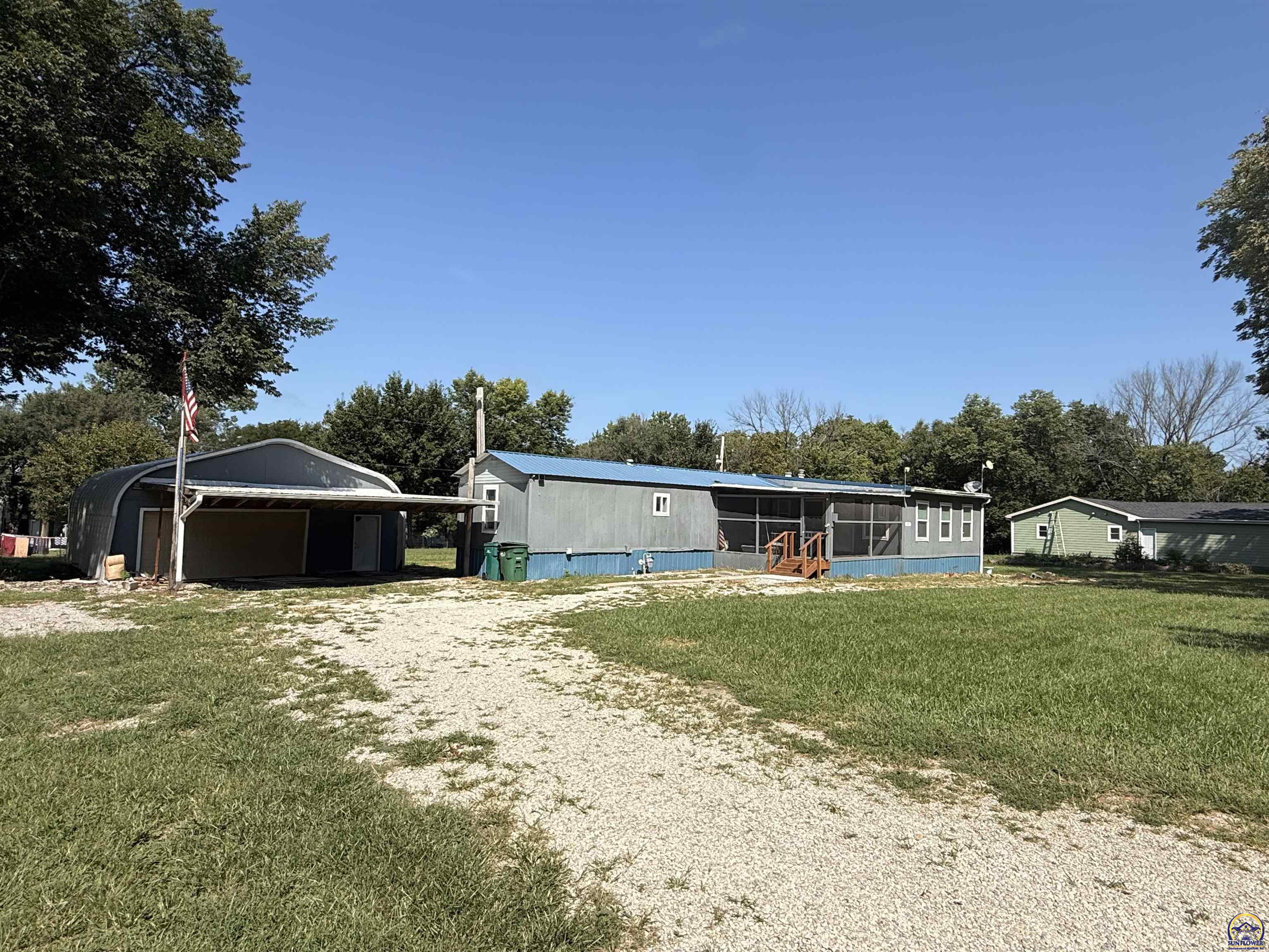 Gray single-story home with a screened porch, detached garage, gravel drive, and small green outbuilding.