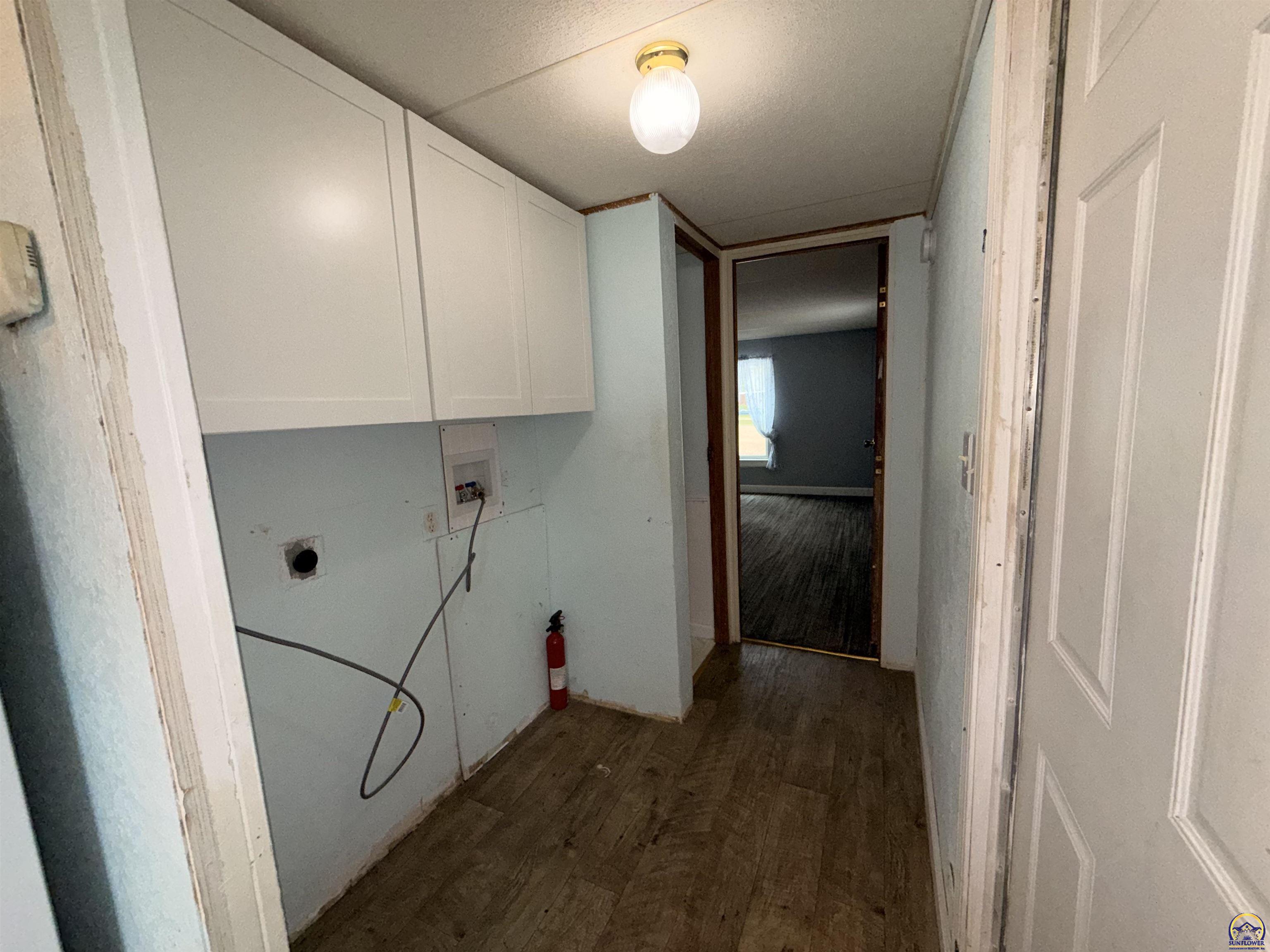 Vacant utility area with upper cabinets, exposed laundry hookups, and worn wood flooring.