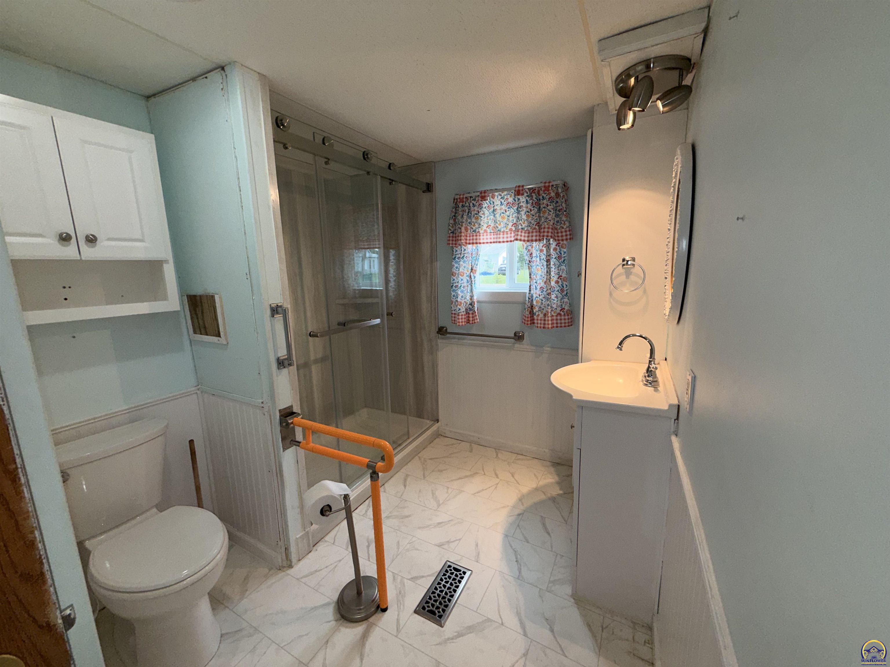 Bathroom with glass walk-in shower, orange support rail, and marble-look tile flooring.