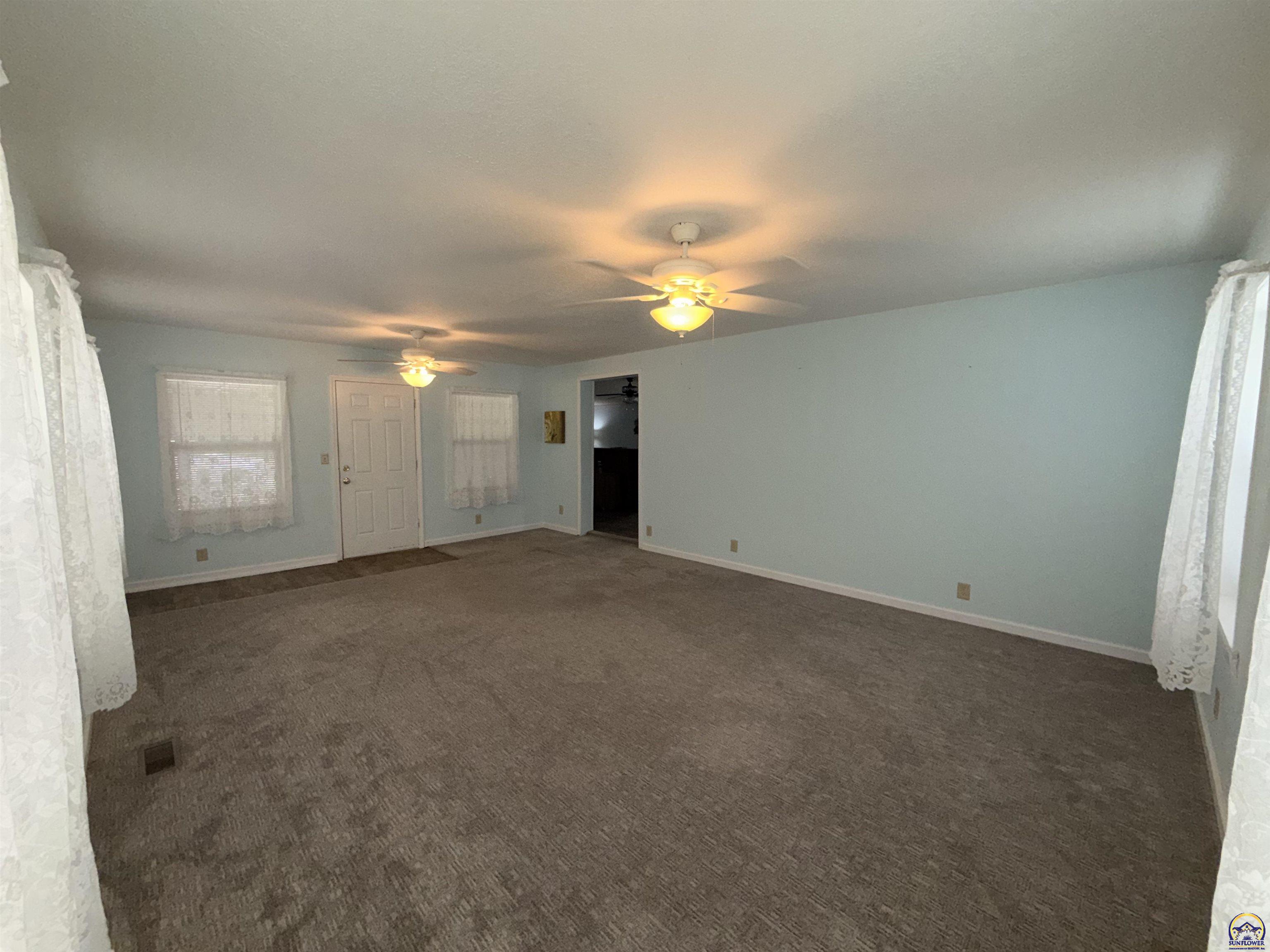 Empty living room with brown carpet, pale blue walls, and two ceiling fans.