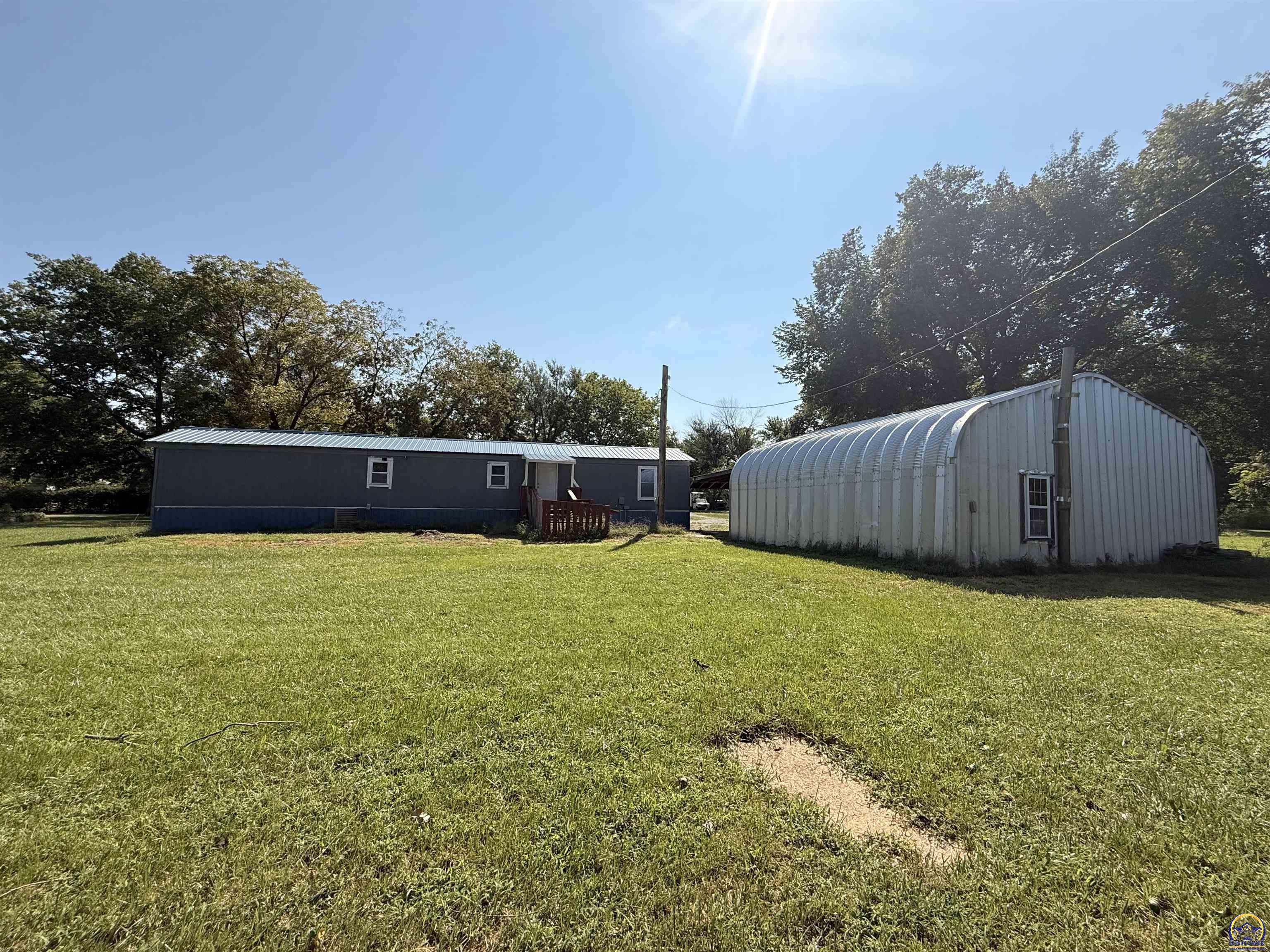 Single-story blue home and large arched metal outbuilding beside a grassy lawn.