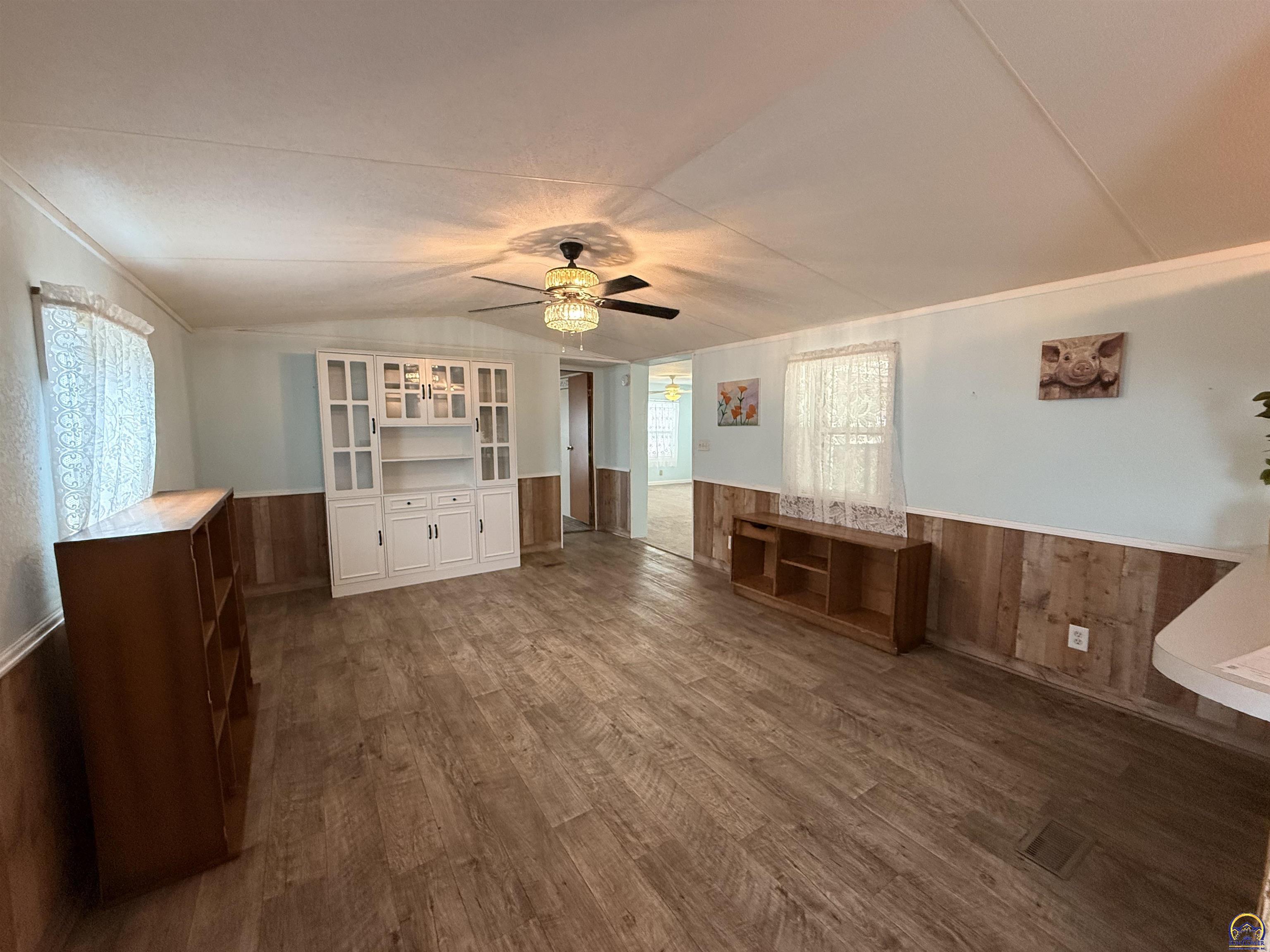Living room with a white built-in cabinet, wood-paneled wainscoting, and a ceiling fan with light.