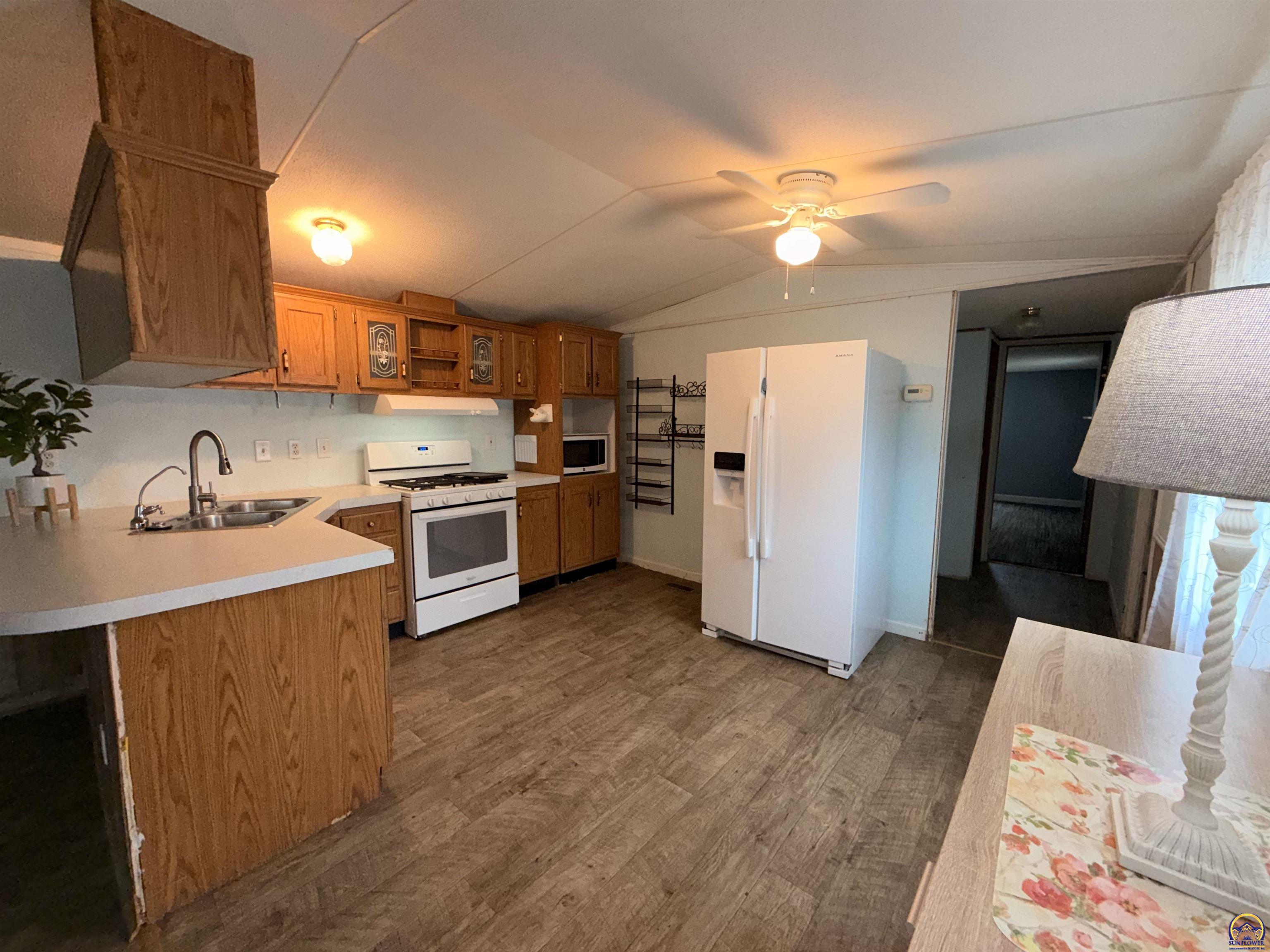Kitchen with wood cabinets, white appliances, a double sink, and wood-look flooring.