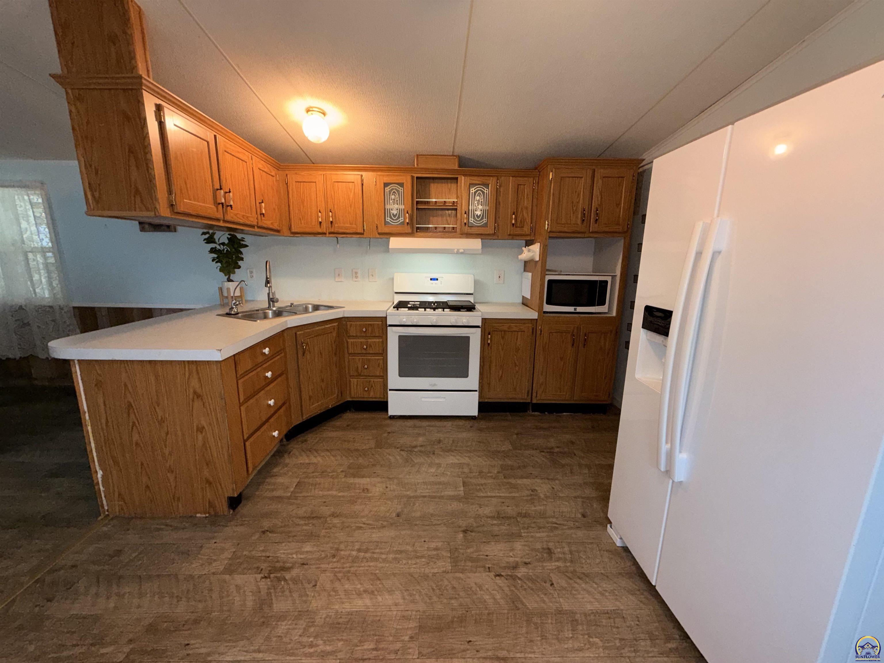 Kitchen with wood cabinets, white appliances, and patterned brown flooring.