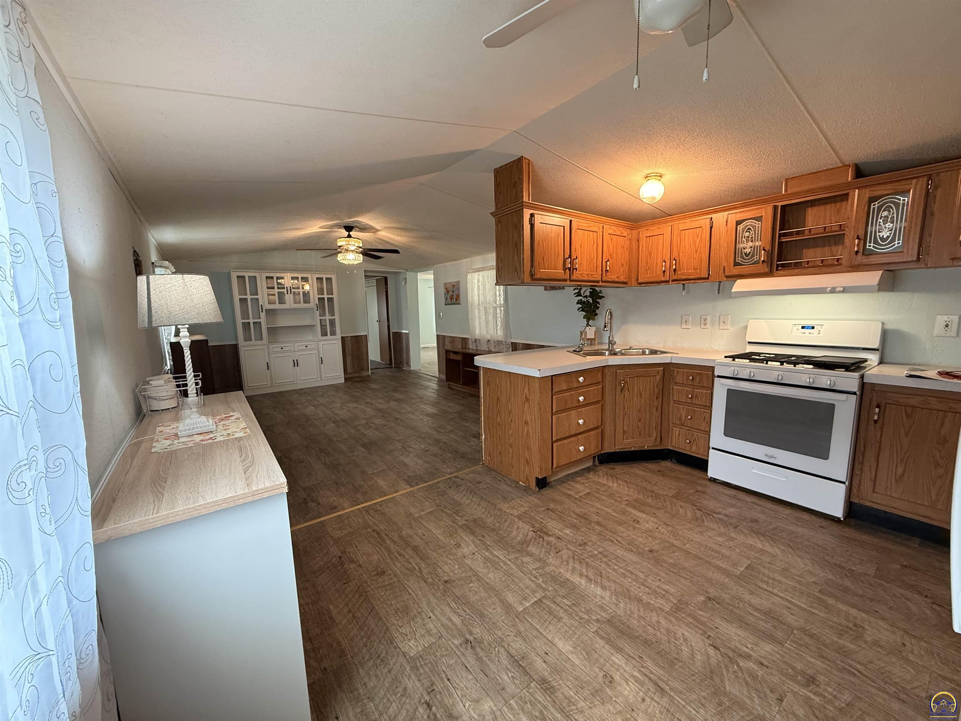 Kitchen with warm wood cabinets, a white gas range, and a peninsula sink opening to a living area.