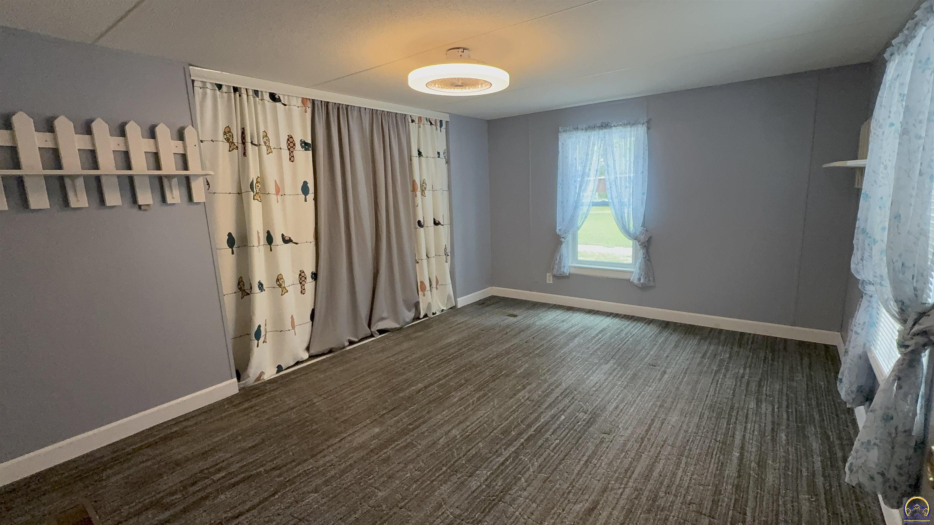 Empty bedroom with gray walls, striped carpet, and bird-patterned curtains.