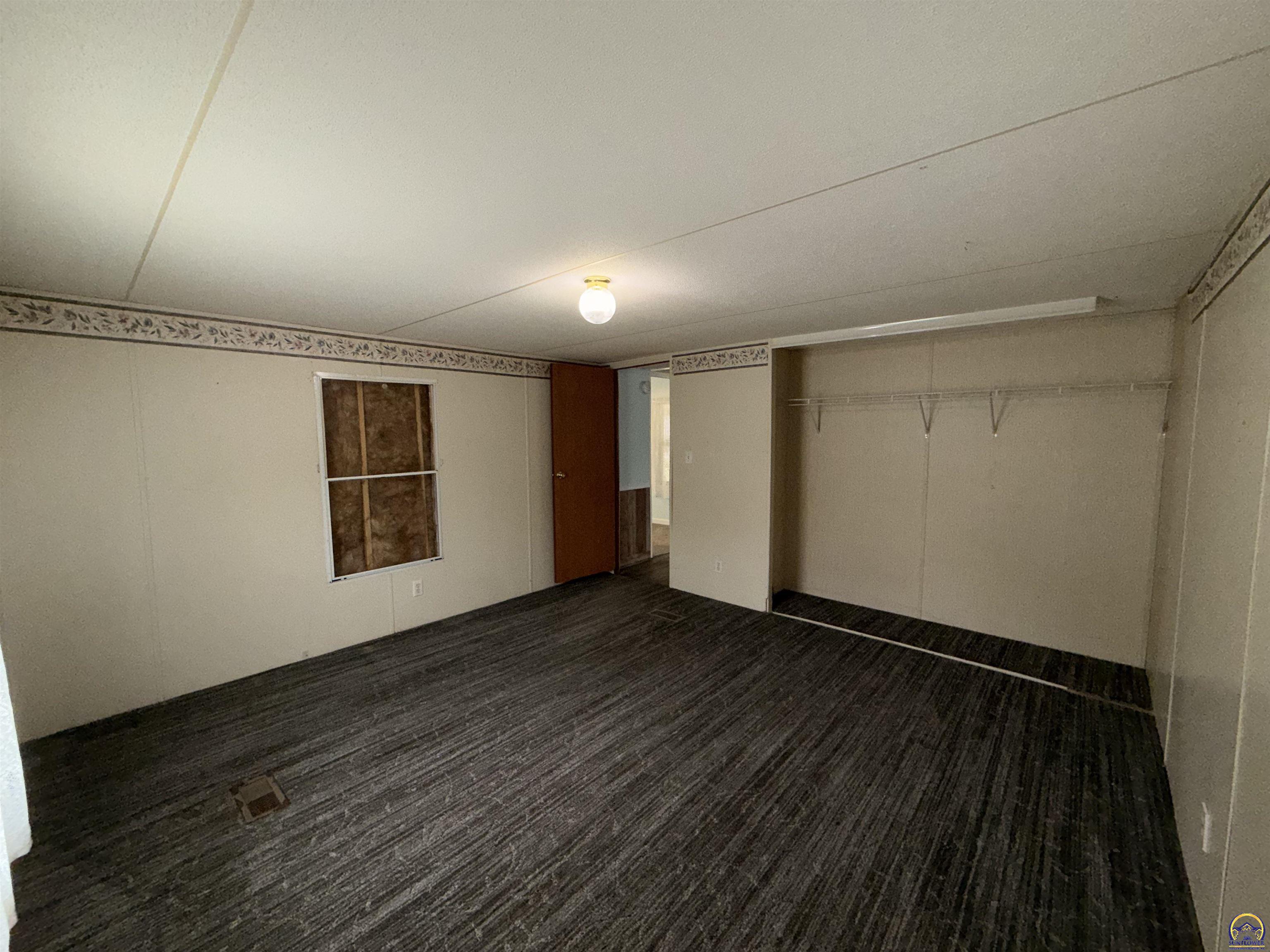 Empty carpeted room with a recessed closet, hanging rod, covered window, and open doorway.