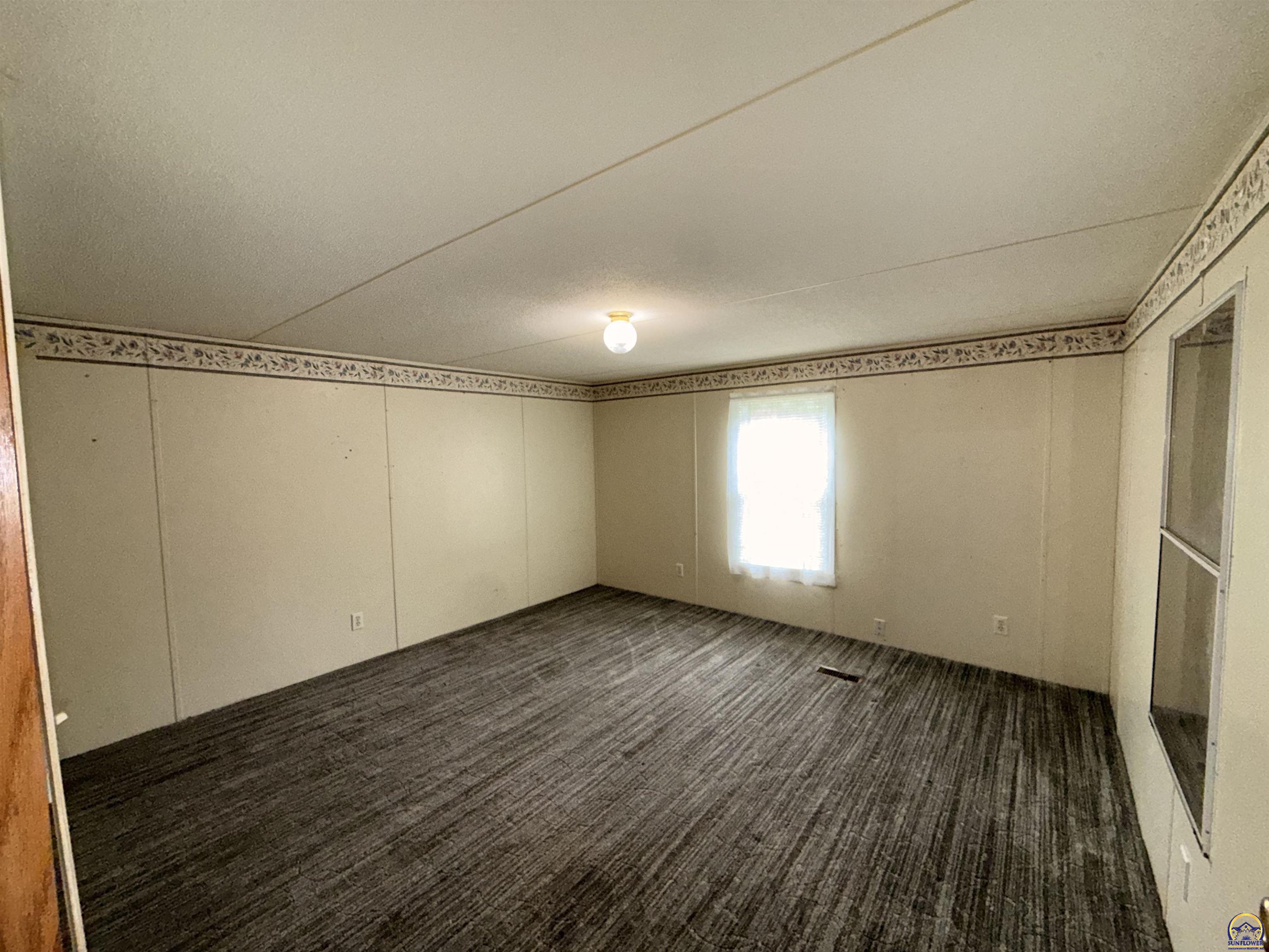 Empty room with dark striped carpet, beige walls, and a window with sheer curtains.