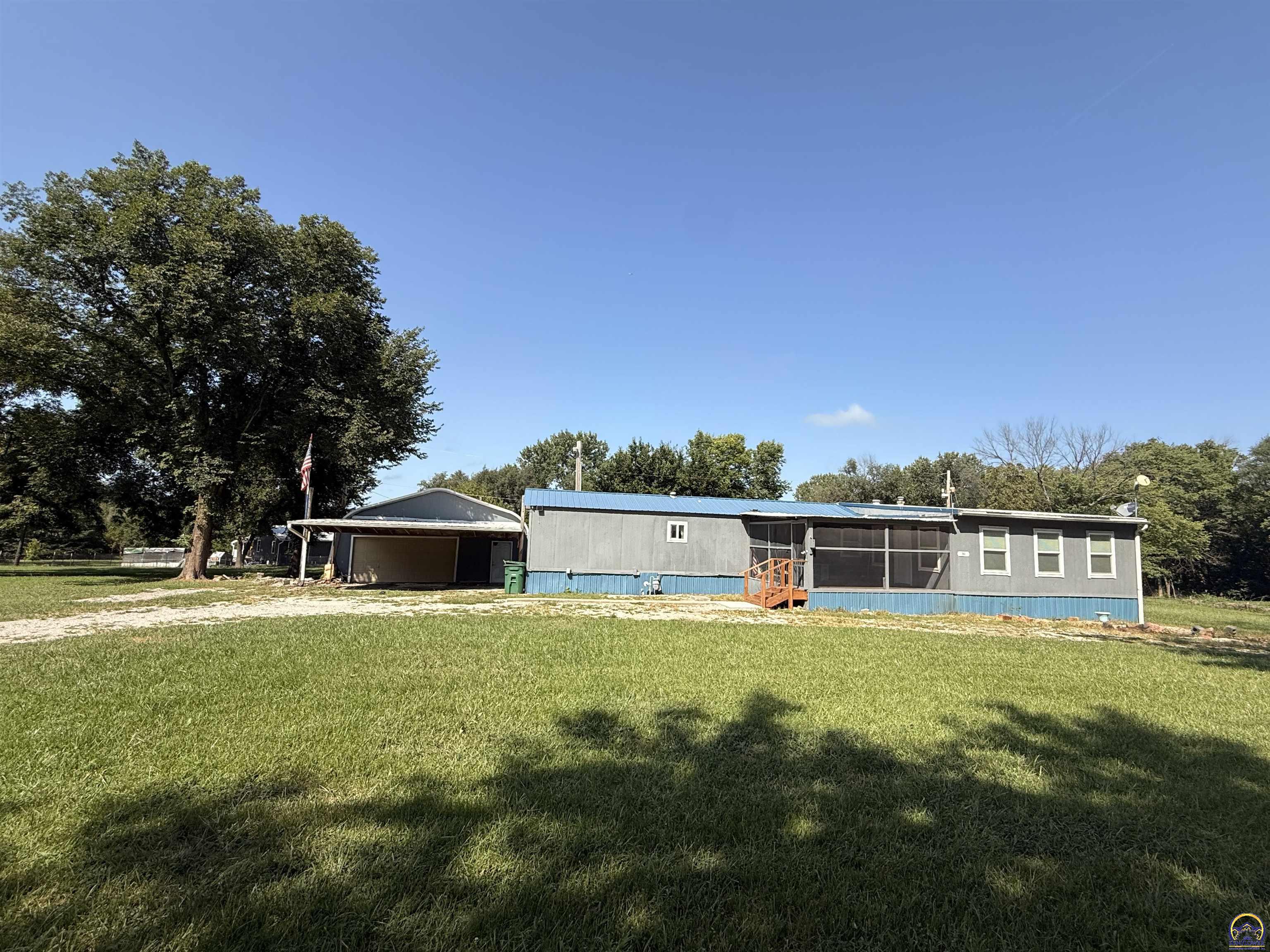 Gray home with blue roof and screened porch on a broad grassy lawn.