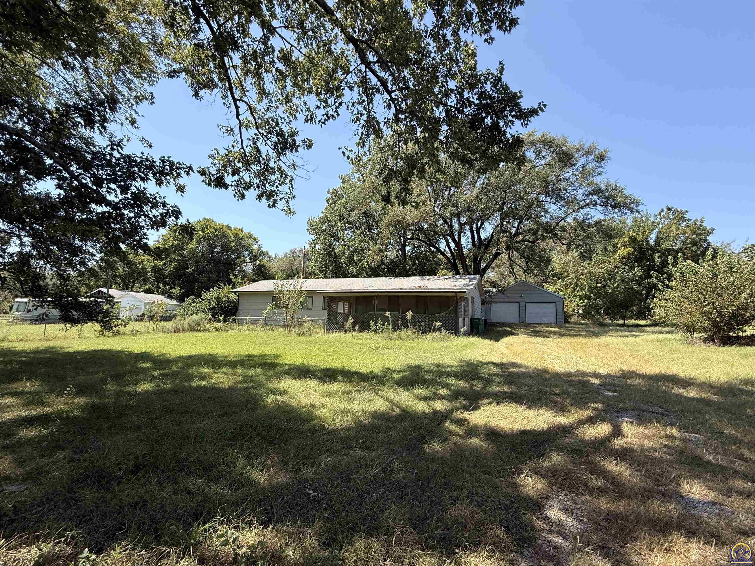 Single-story house and detached garage beyond a broad, tree-shaded grassy yard.