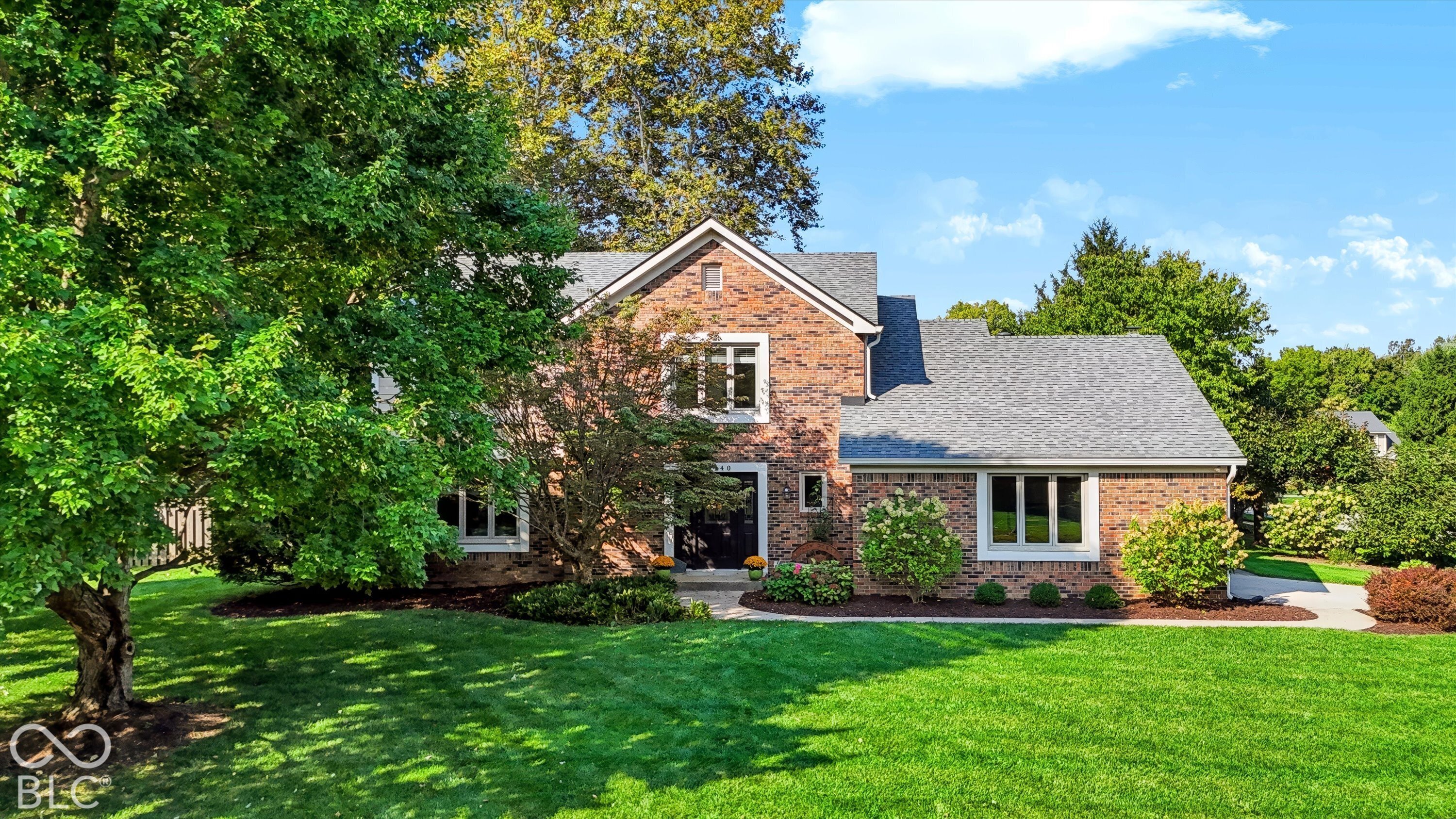 Brick home with gray gabled roofs, mature trees, and a landscaped front lawn.