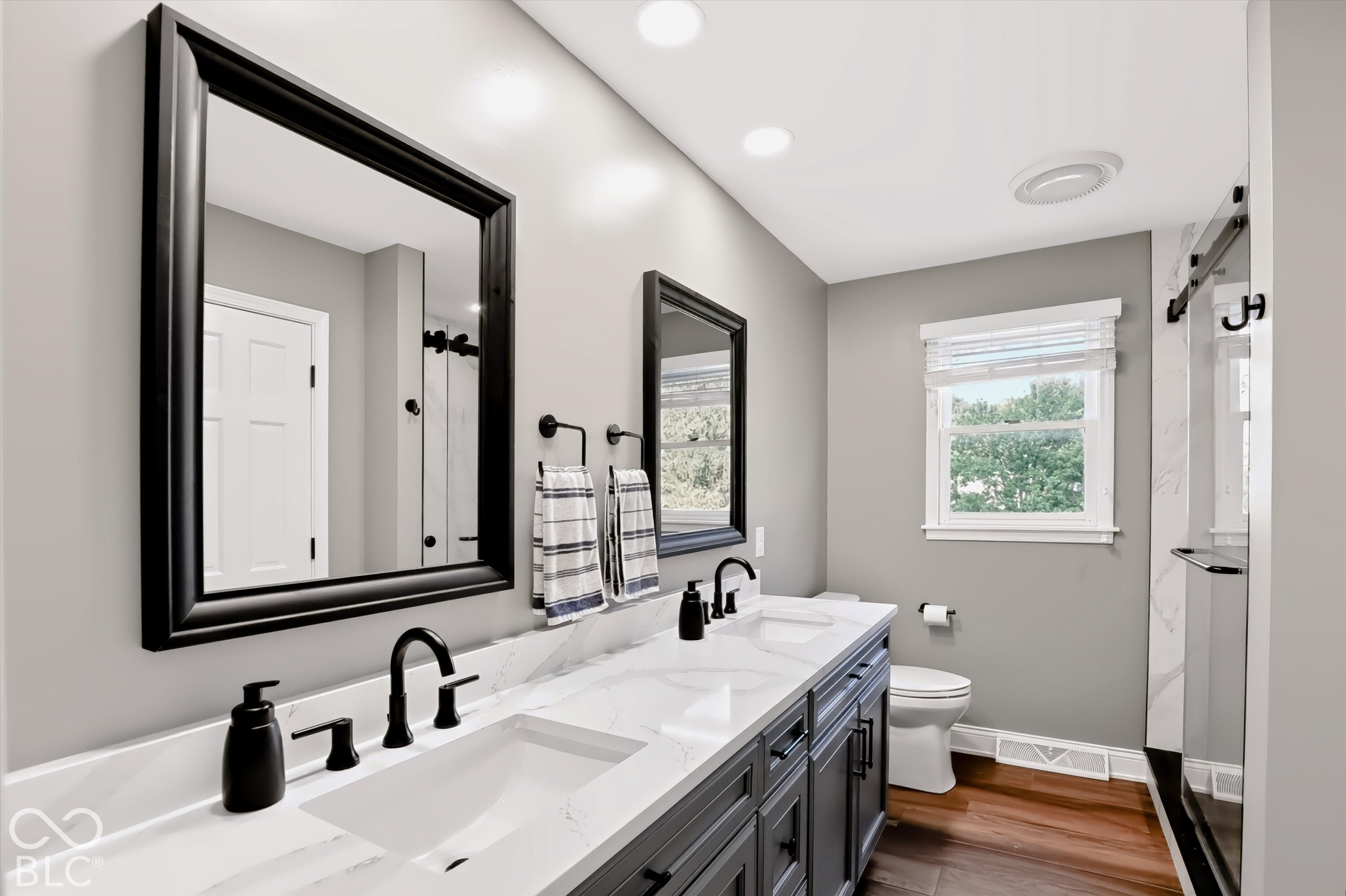 Bathroom with a dark double vanity, marble-look counters, black fixtures, and a glass shower.