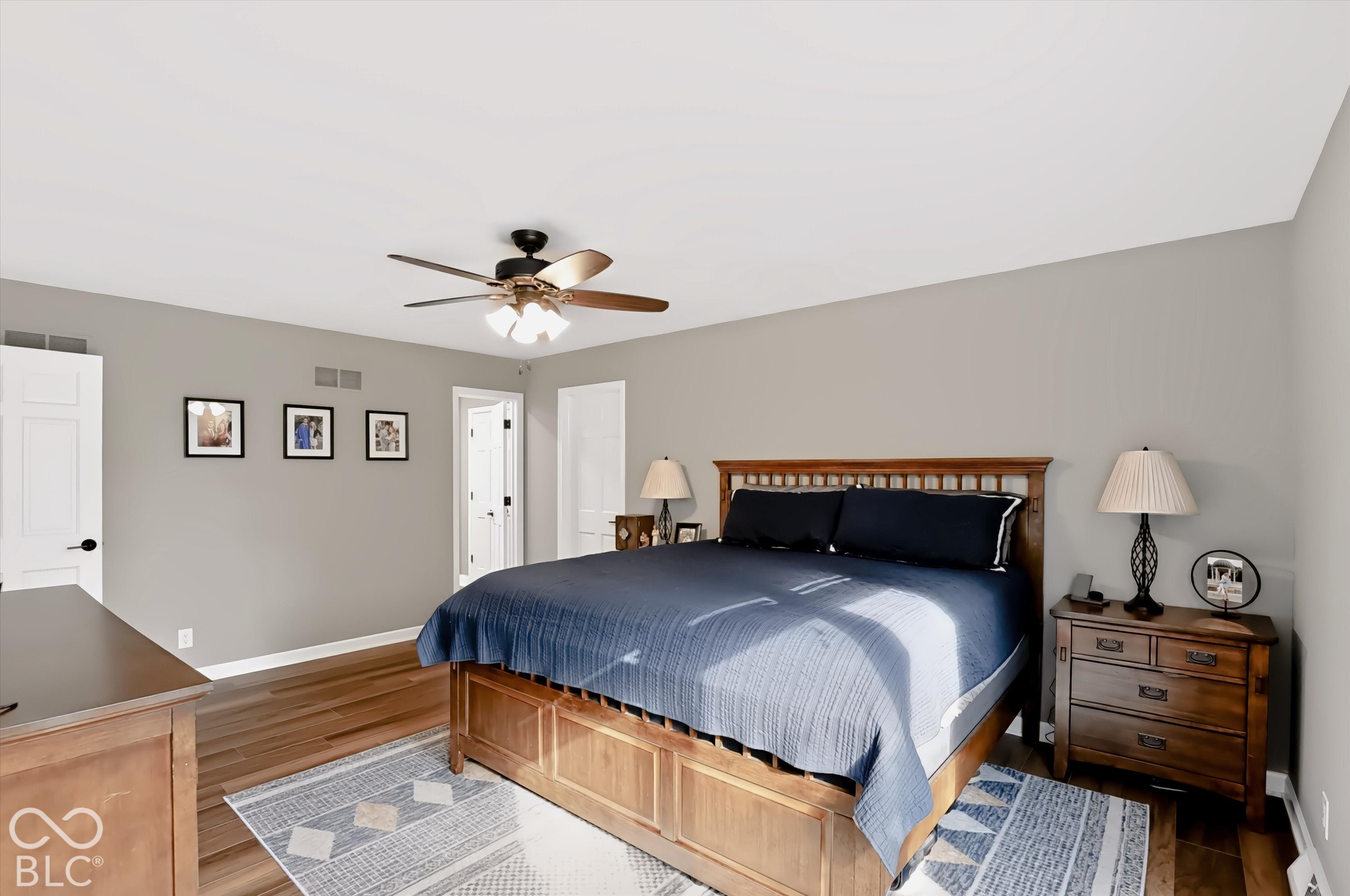 Bedroom with a wooden bed, navy bedding, matching furniture, and a ceiling fan.
