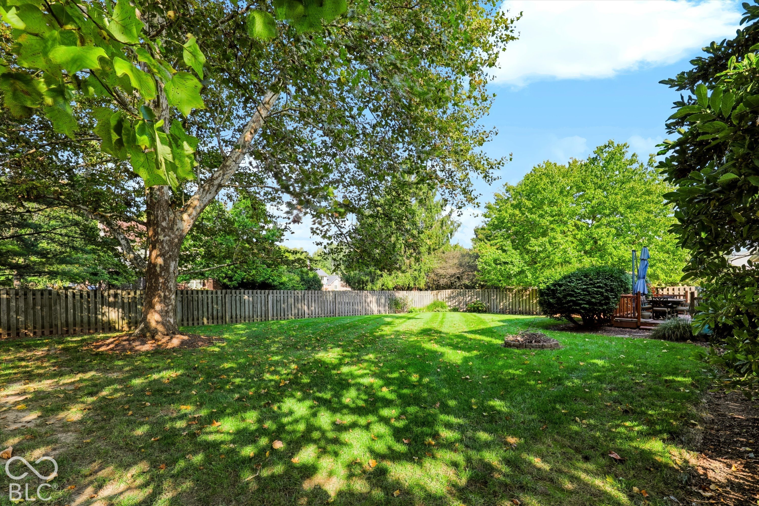 Fenced backyard with a broad lawn, mature shade trees, and a raised deck with patio furniture.