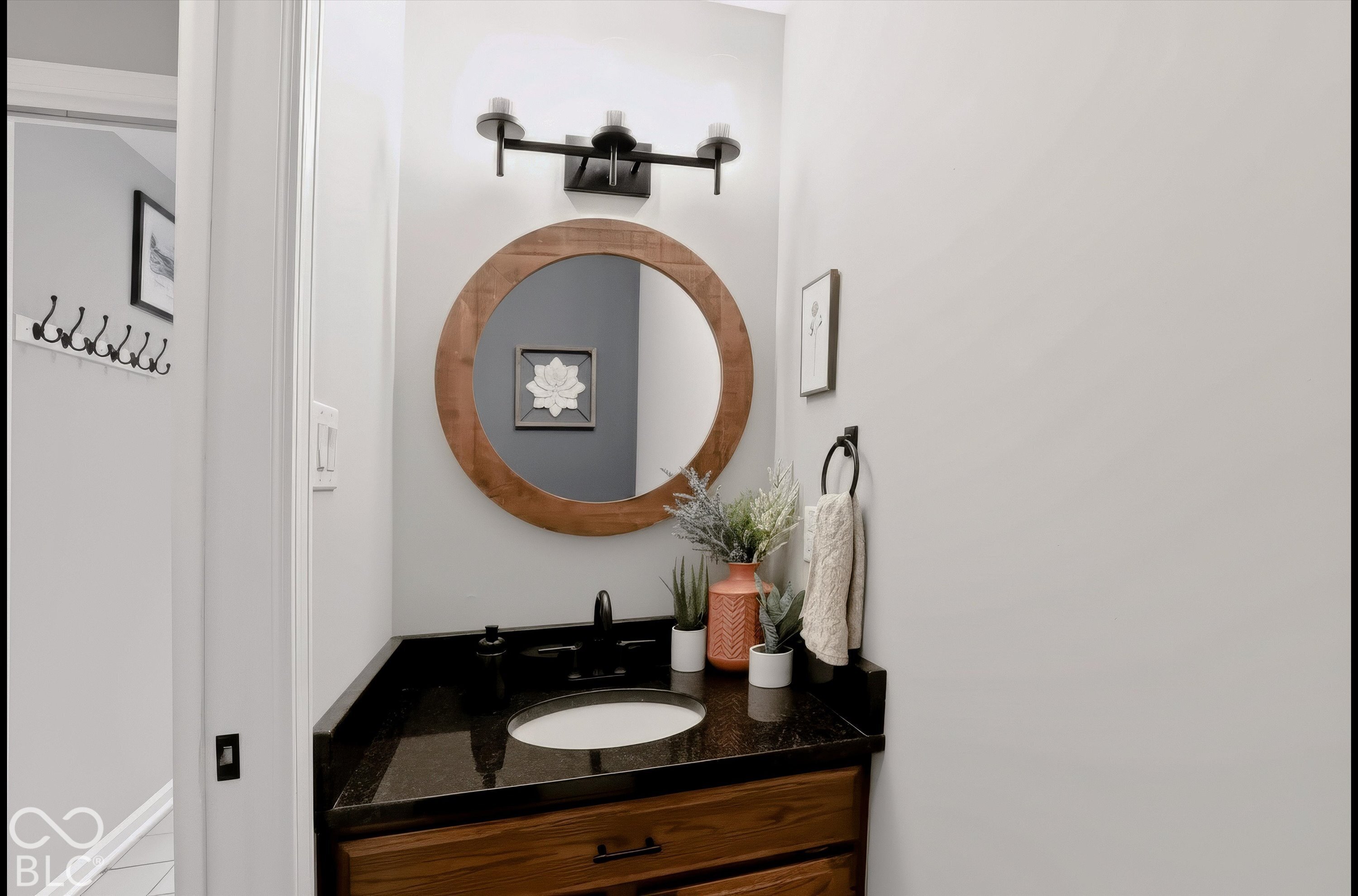 Powder room vanity with a round wood-framed mirror, black countertop, and warm wood drawers.