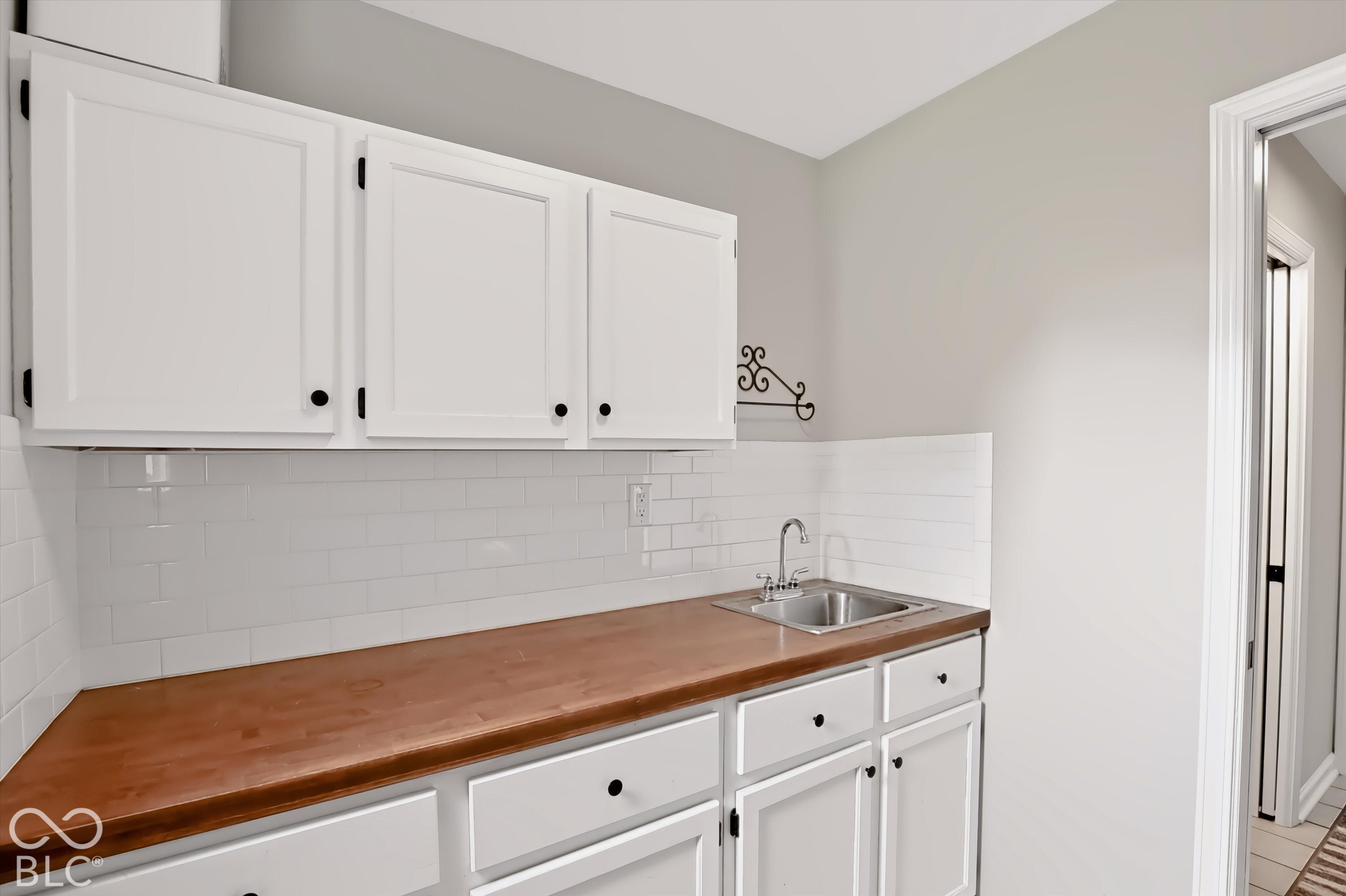 Utility room with white cabinets, a long brown counter, and a small stainless-steel sink.