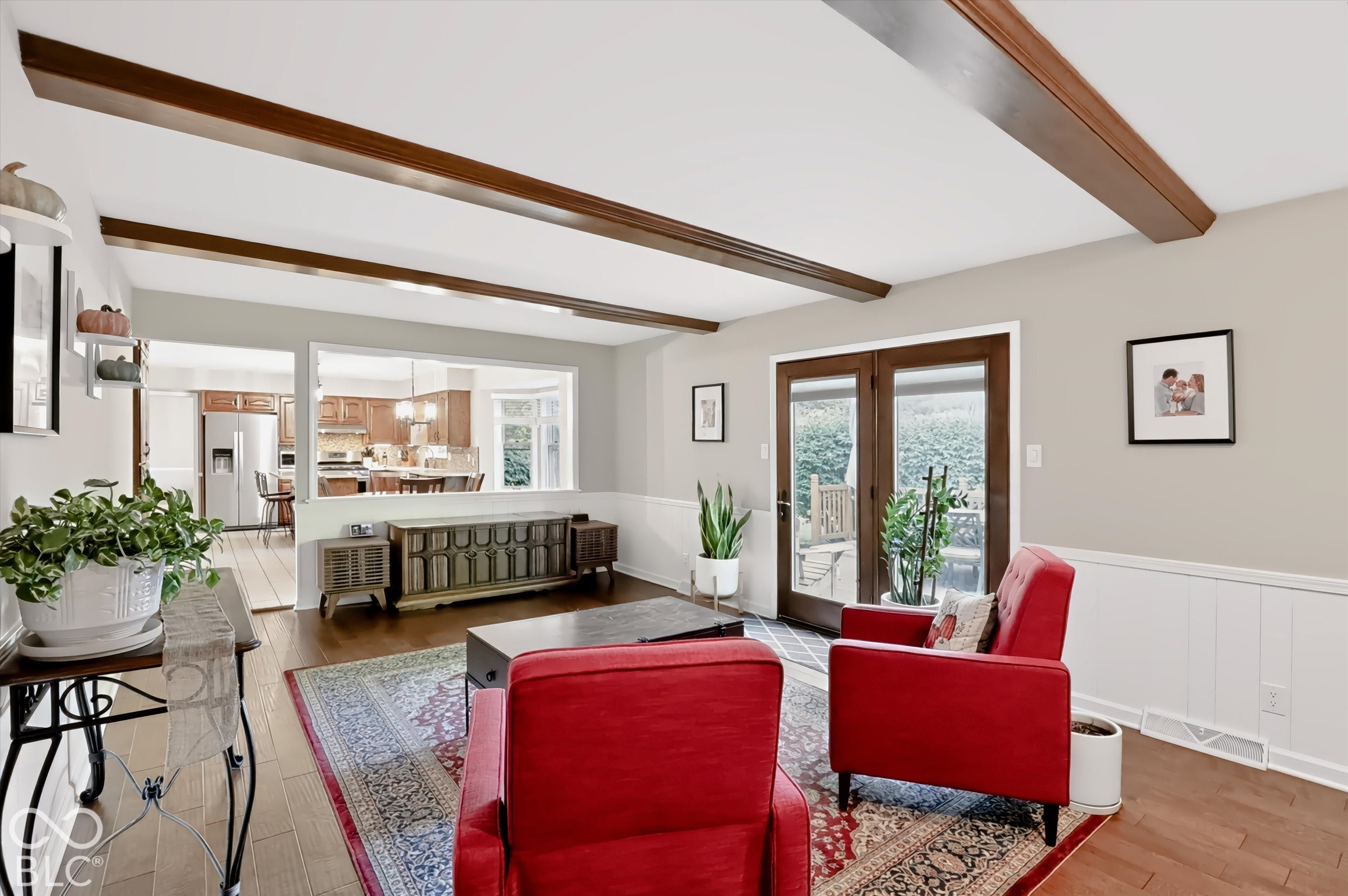 Living room with exposed wood beams, red armchairs, and a pass-through to the kitchen.