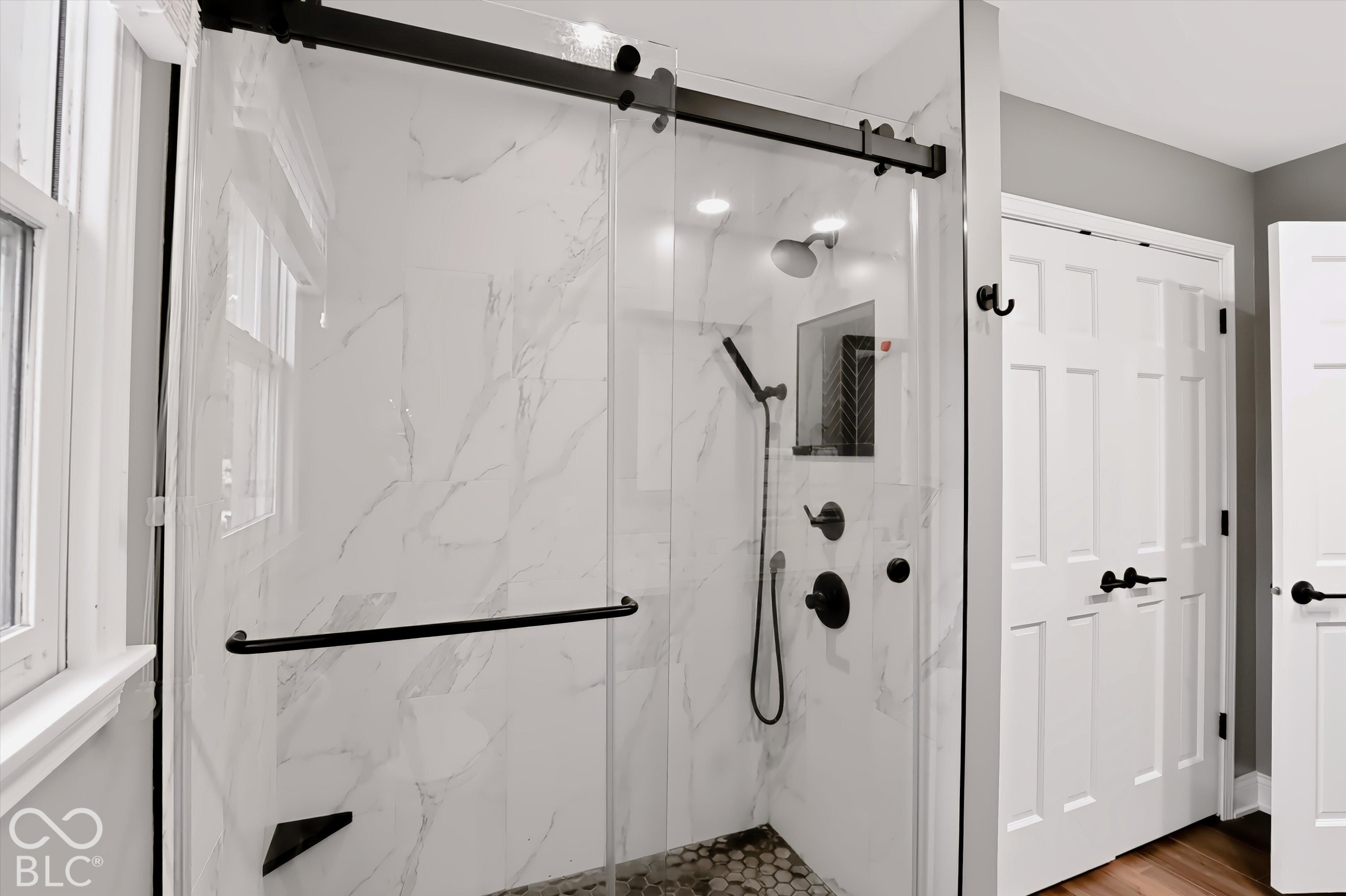 Bathroom with a glass-enclosed marble-look shower, black fixtures, and pebble mosaic floor.