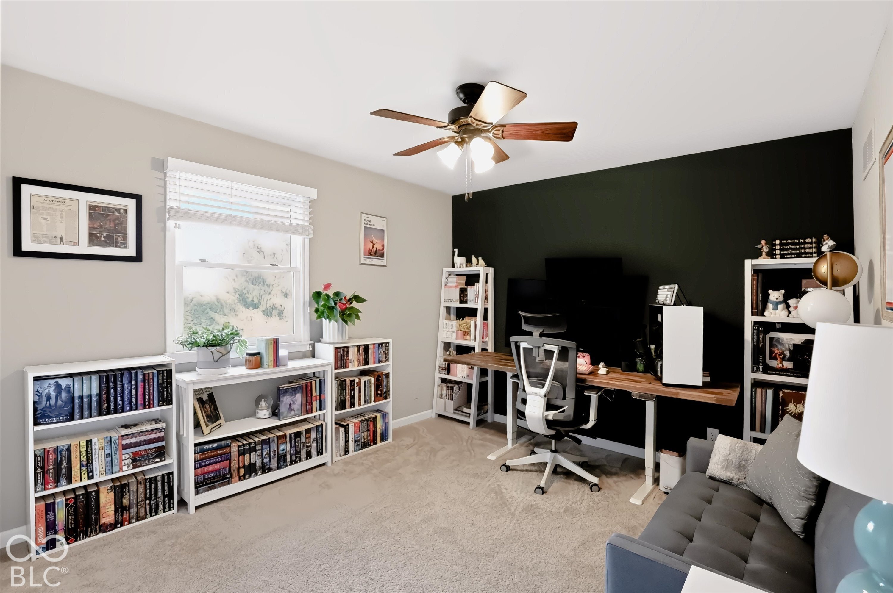 Furnished home office with a long desk, dark accent wall, bookcases, and gray sofa.