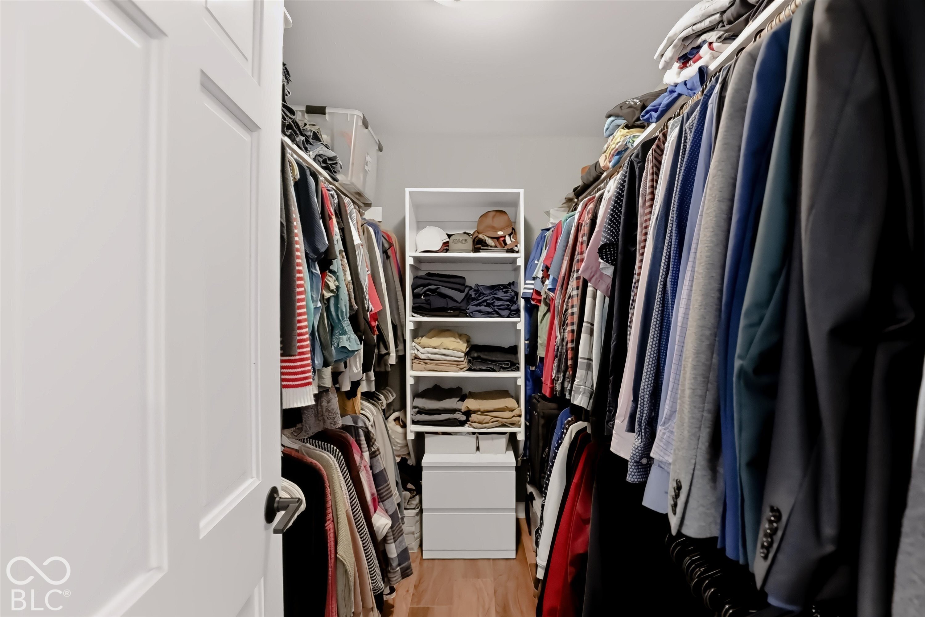 Walk-in closet lined with hanging clothes and white shelving filled with folded garments.