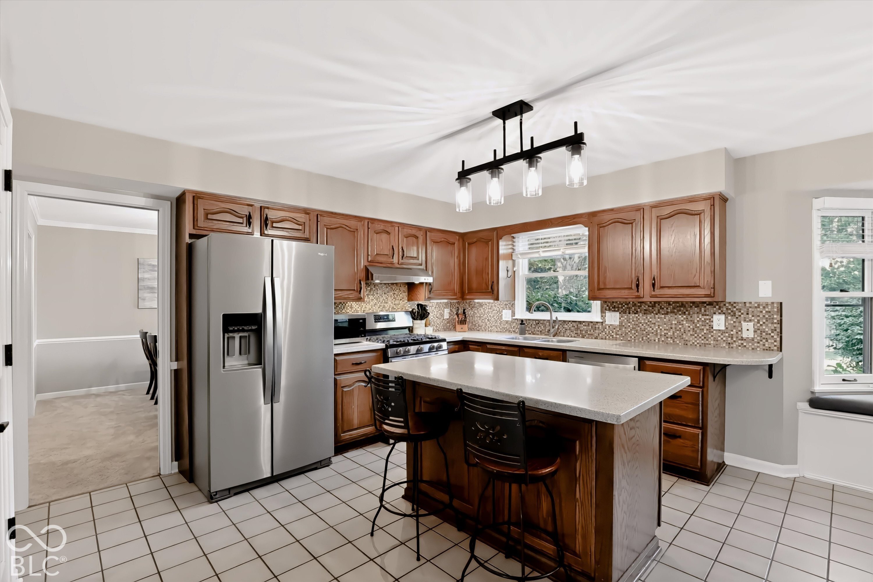 Kitchen with warm wood cabinets, mosaic backsplash, and a large island with two bar stools.