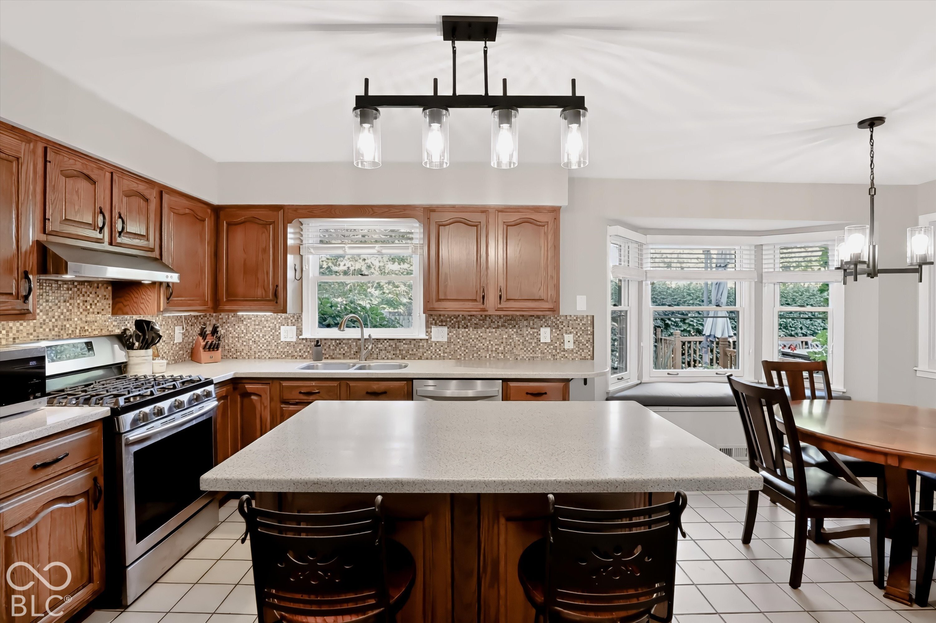 Kitchen with warm wood cabinets, a large white island, and a dining area beside a bay window.