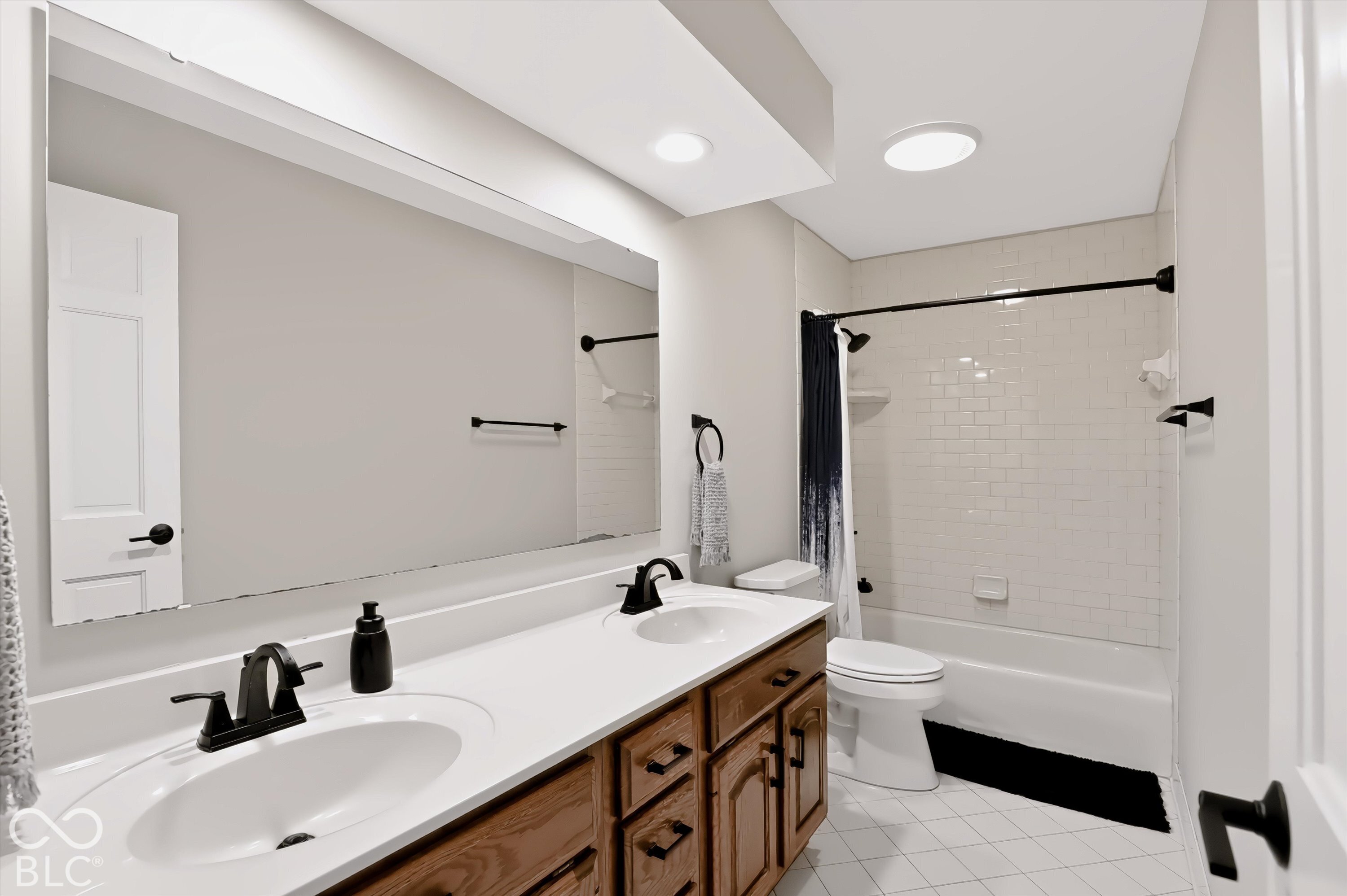 Bathroom with a long double vanity, wood cabinets, black faucets, and a tiled tub-shower.