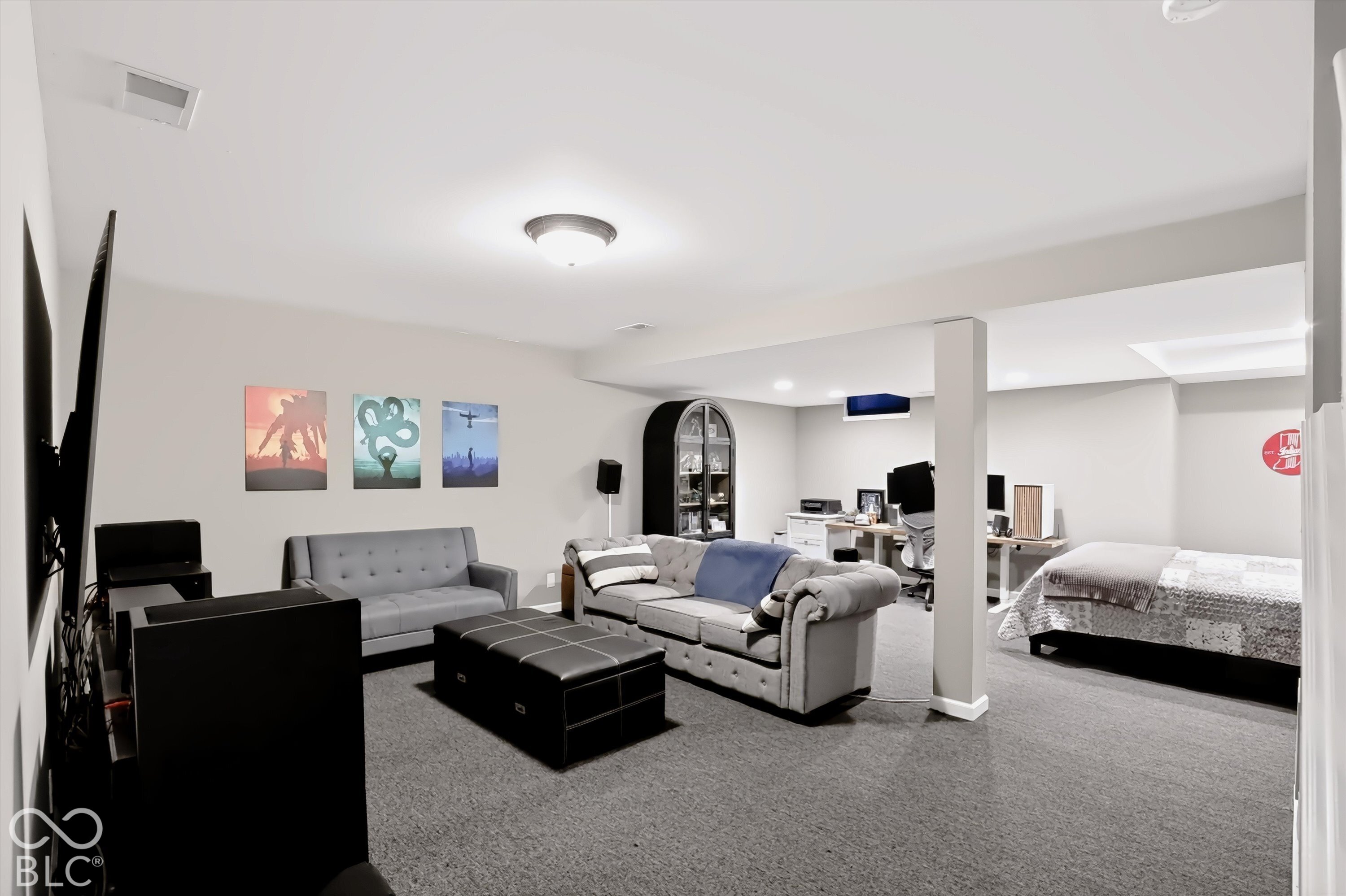 Furnished basement sitting area with gray sofas, a desk workspace, and an adjoining bed.