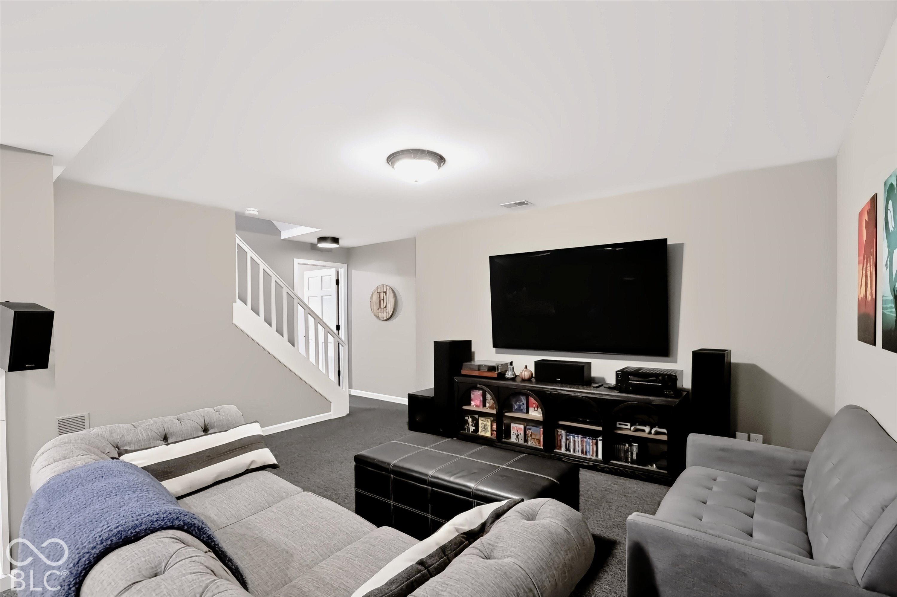 Basement media room with gray sectional sofas, a large television, and a staircase.