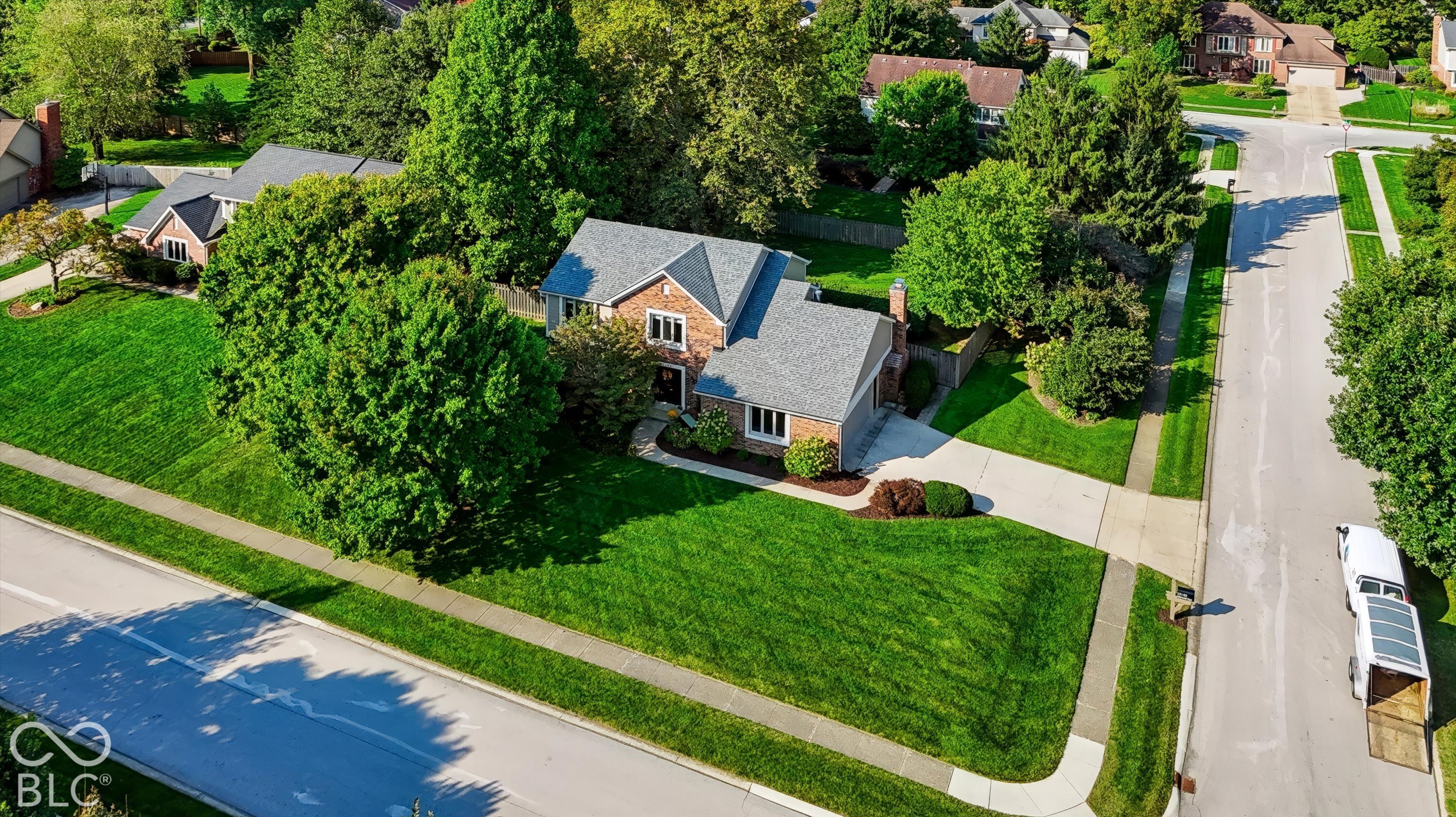 Brick house on a leafy corner lot with a broad lawn and driveway, viewed from above.
