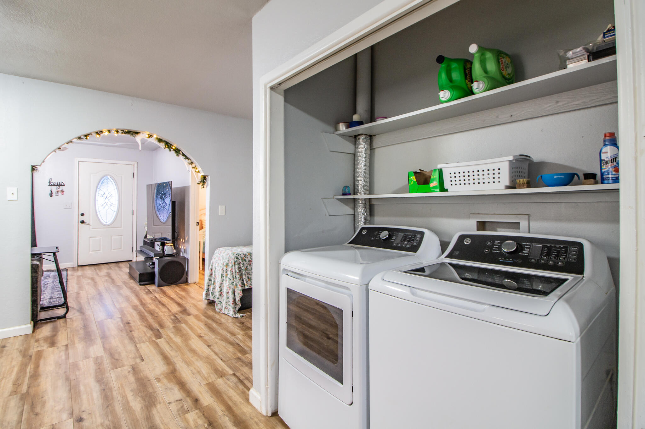 Laundry room with white washer and dryer, open shelves, and a view into the adjoining living area.