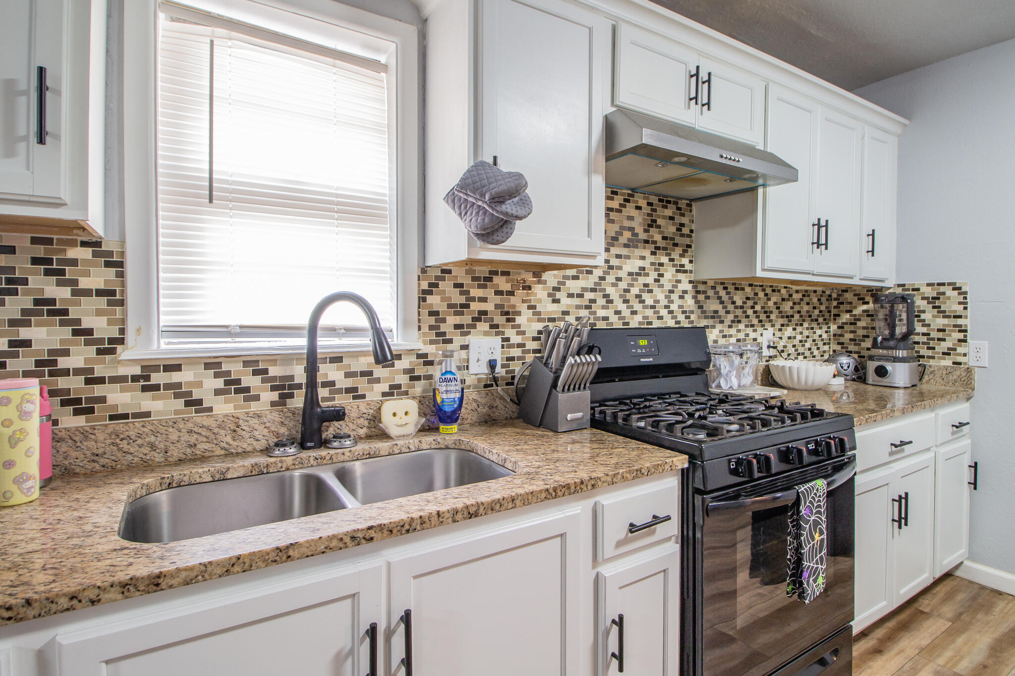 Kitchen with white cabinets, granite counters, mosaic tile backsplash, double sink, and black gas range.