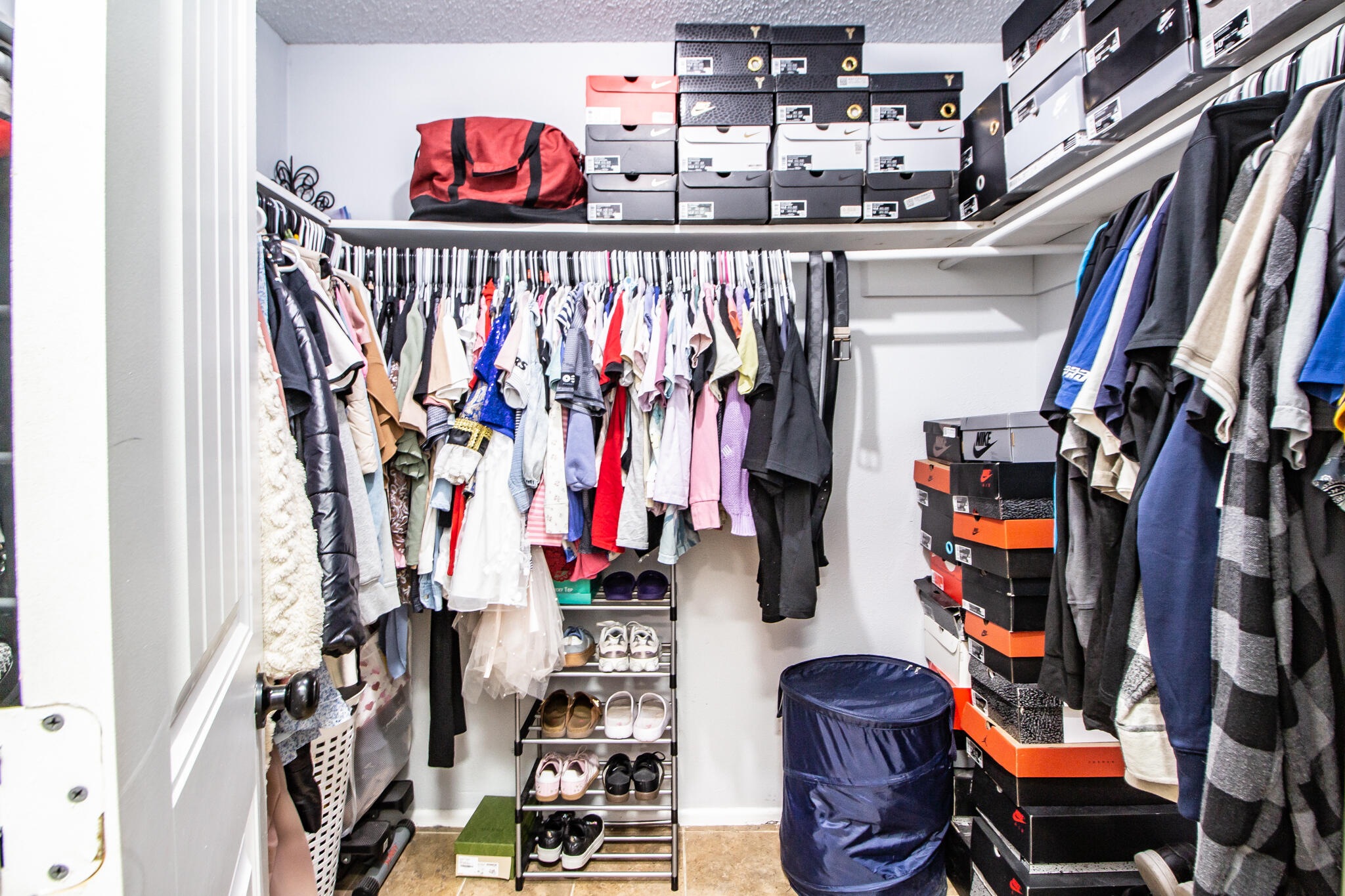 Walk-in closet with crowded clothing racks, stacked shoeboxes, and a shoe rack.