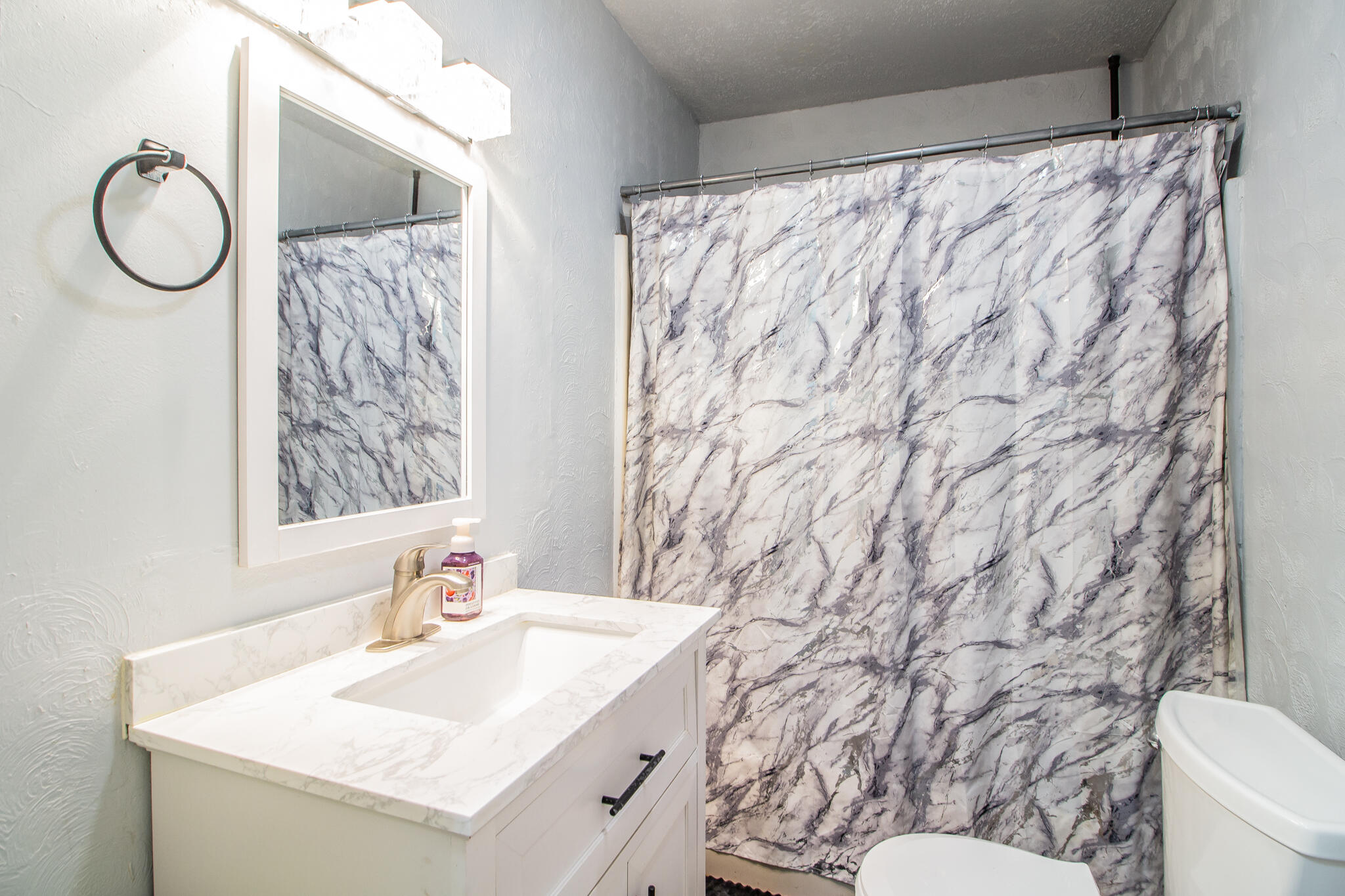 Bathroom with a white vanity, framed mirror, and gray-and-white marble-pattern shower curtain.