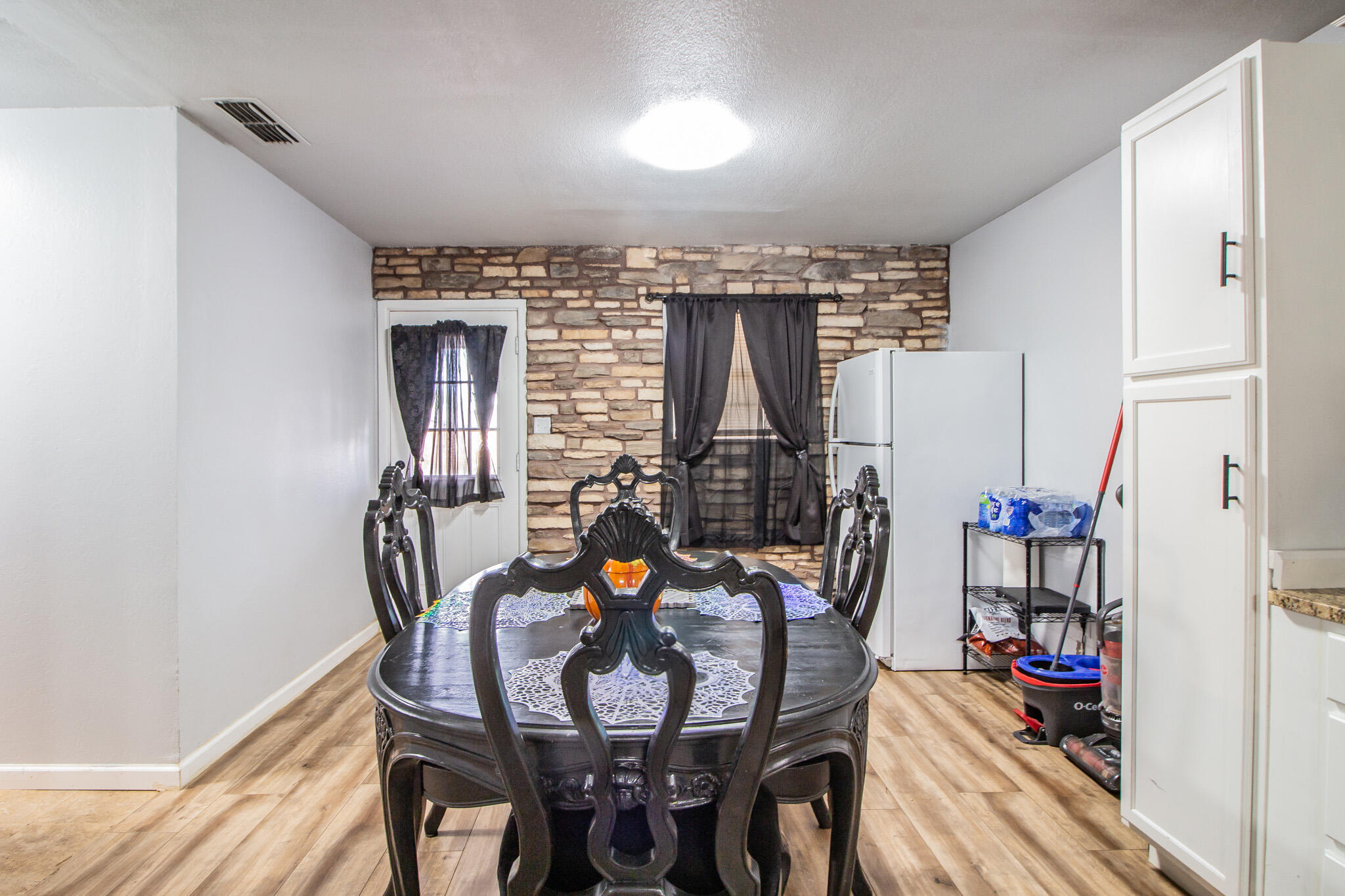 Dining area with an ornate dark table, wood-look flooring, and a stone accent wall.