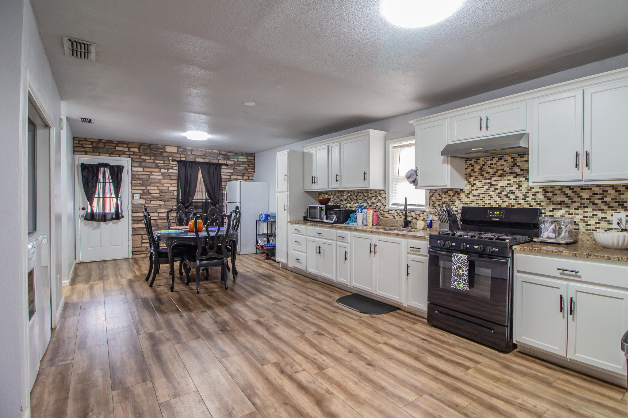 Kitchen and dining area with white cabinets, mosaic backsplash, and a dining table beside a stone accent wall.