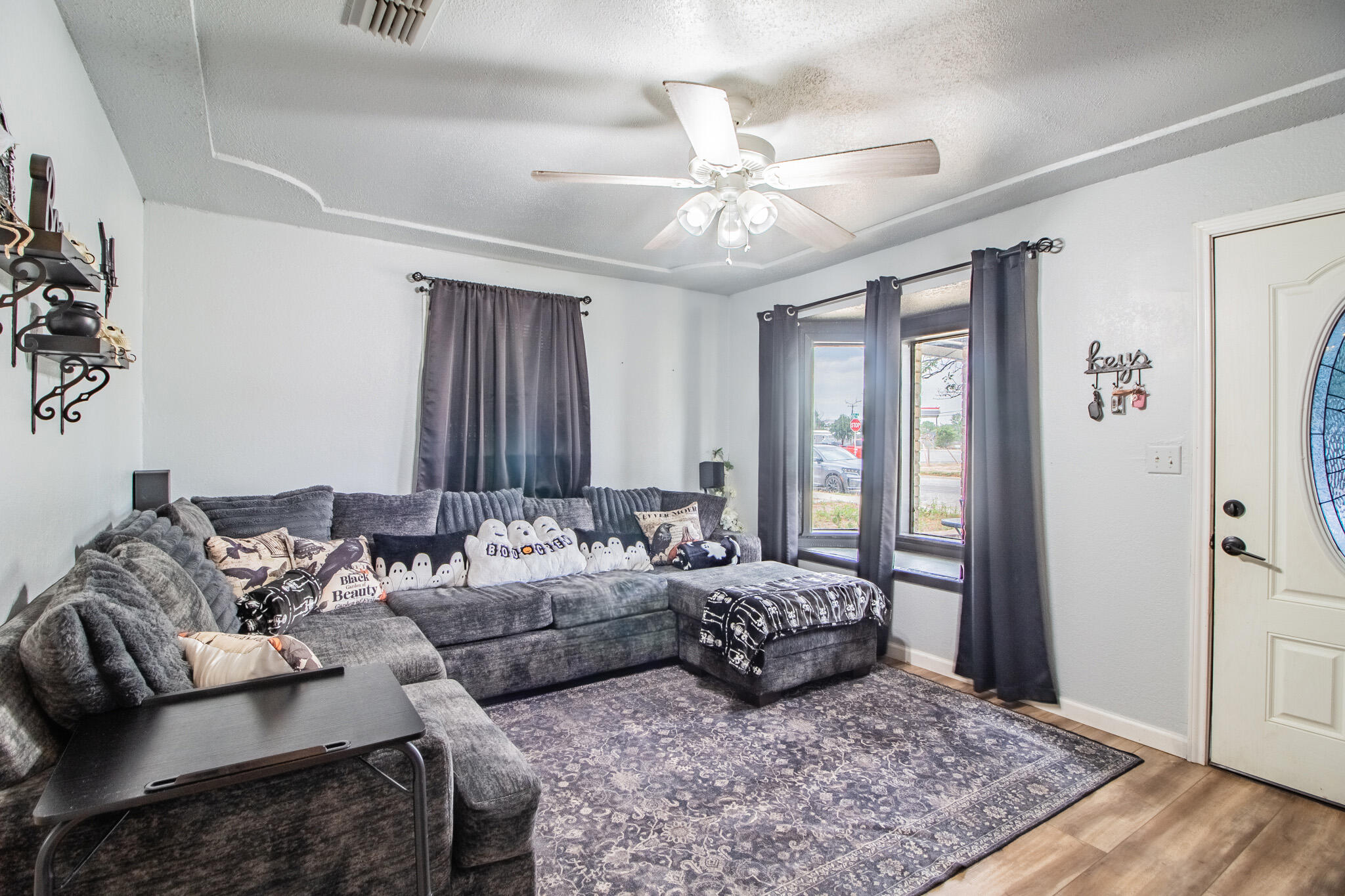 Living room with a gray sectional, patterned rug, ceiling fan, and tall curtained windows.