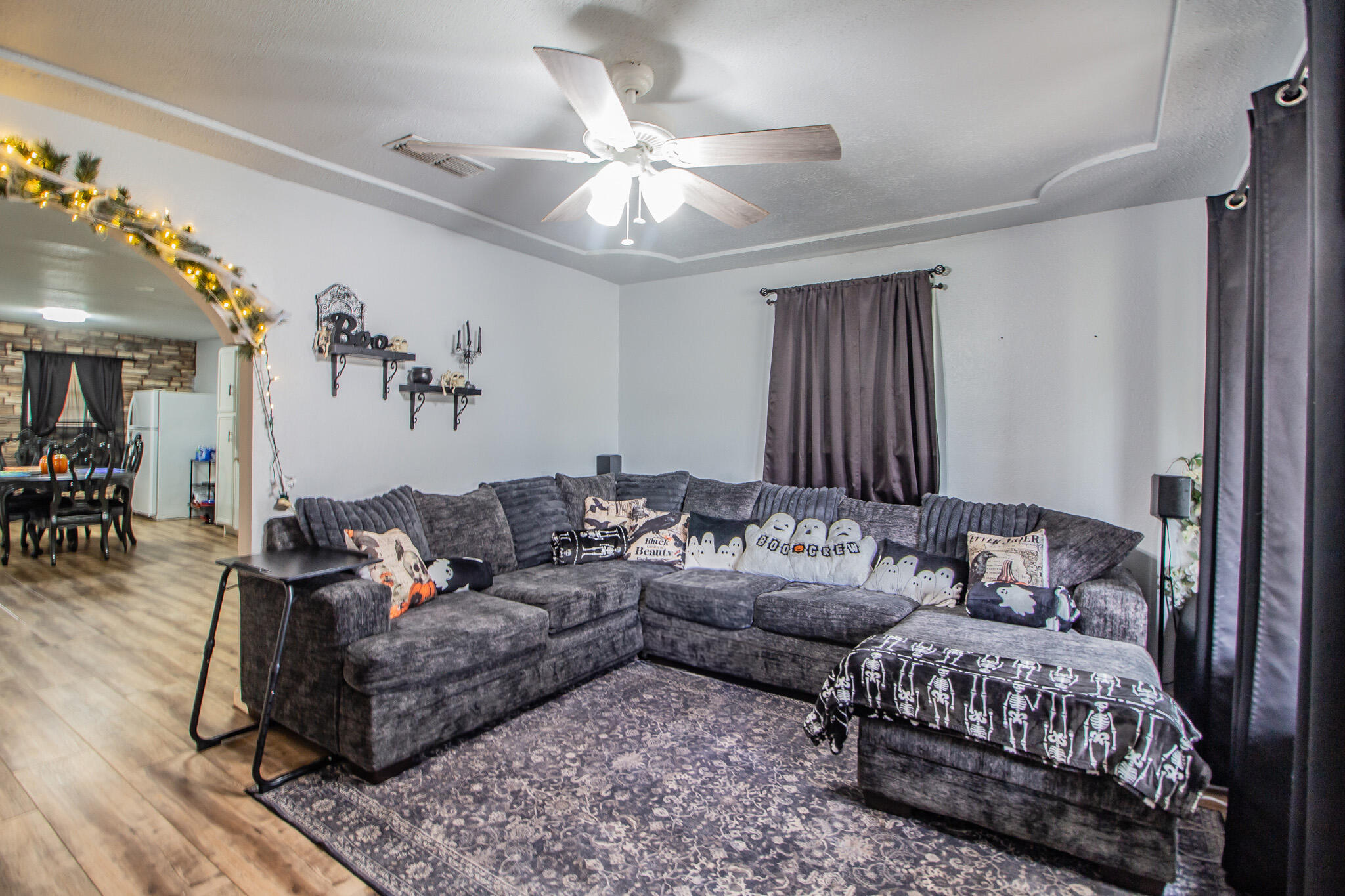 Living room with a dark gray sectional, Halloween pillows, and an arched opening to the dining area.