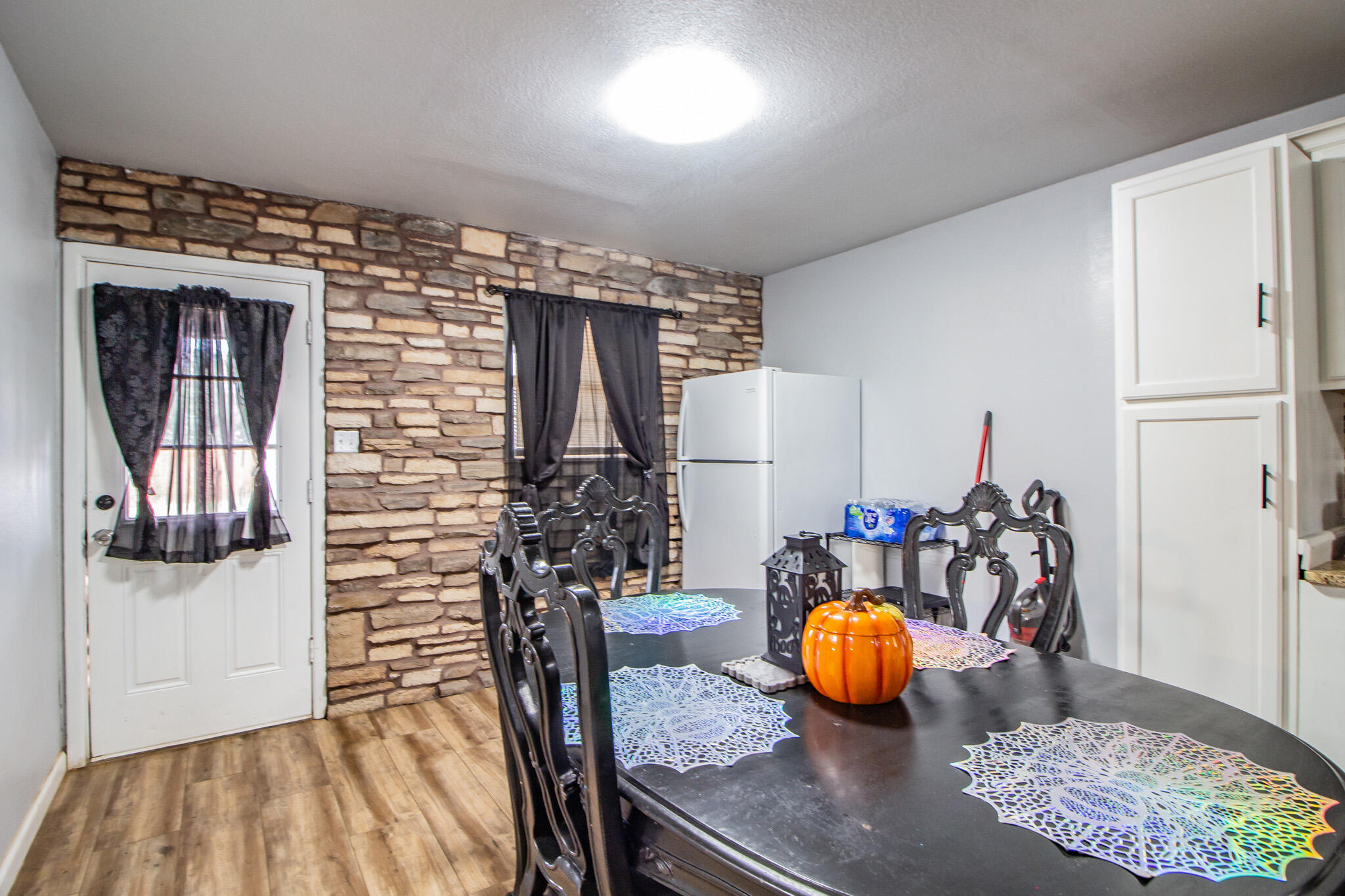 Dining area with a black table, ornate chairs, stone accent wall, and pumpkin centerpiece.